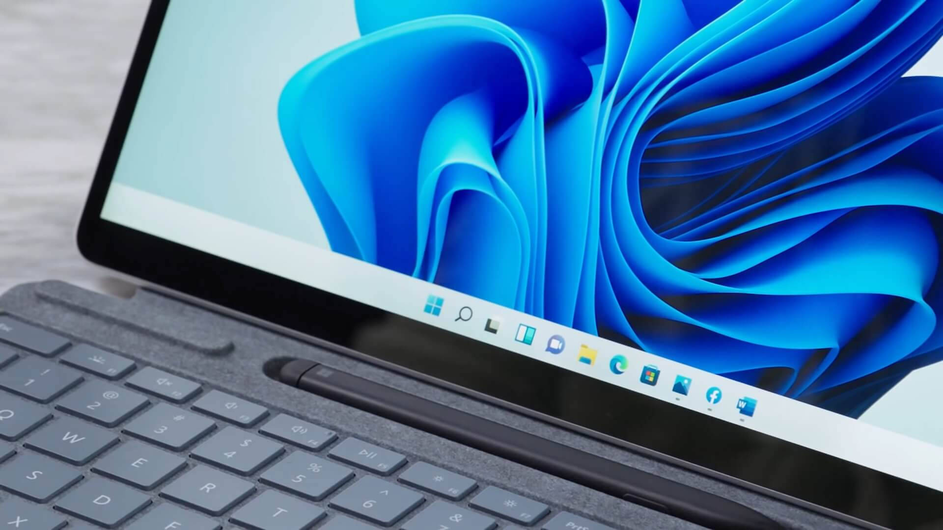Windows 11 Surface Pro 壁紙 — 手提電腦特寫，顯示帶有工作列圖示的動態藍色抽象桌布。