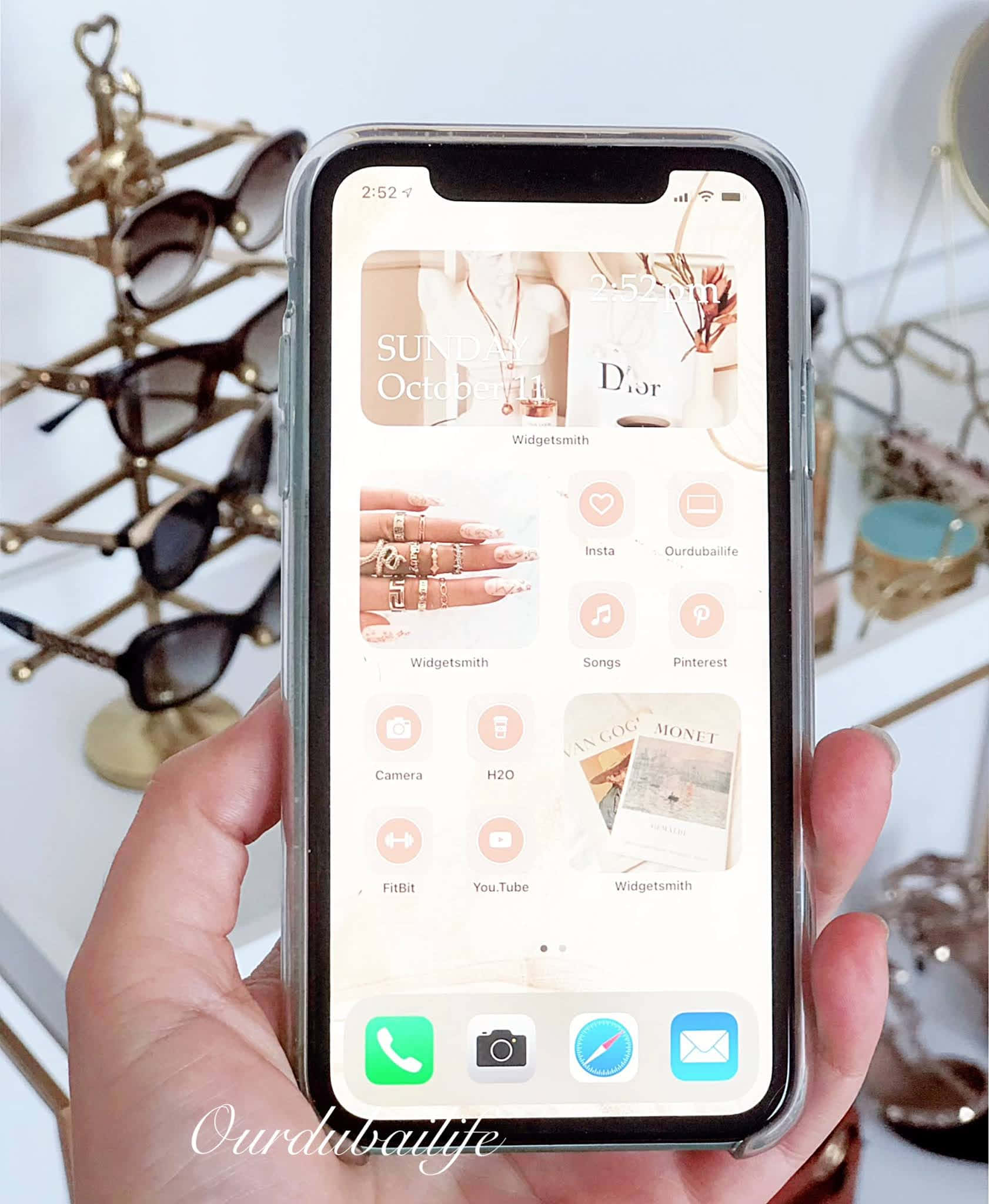 iPhone風格壁紙 桌布 壁紙 — 手握住手機，展示時尚簡約的桌布，帶有時尚小工具和應用程式圖標，背景為金色太陽眼鏡。