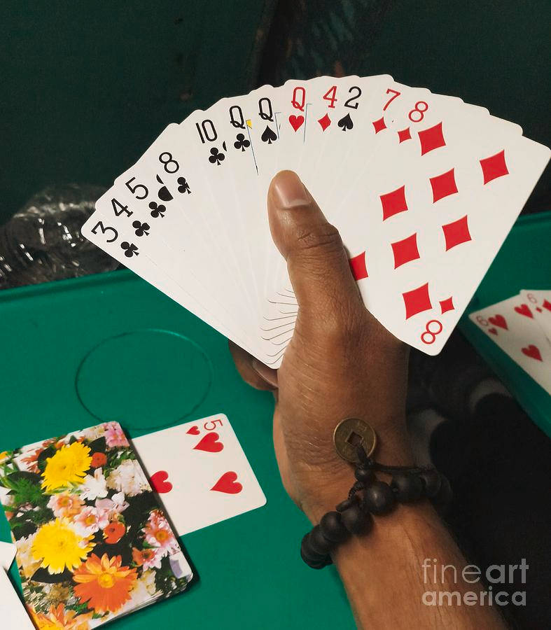 一隻手在綠色遊戲桌上握著扇形攤開的啤牌。
