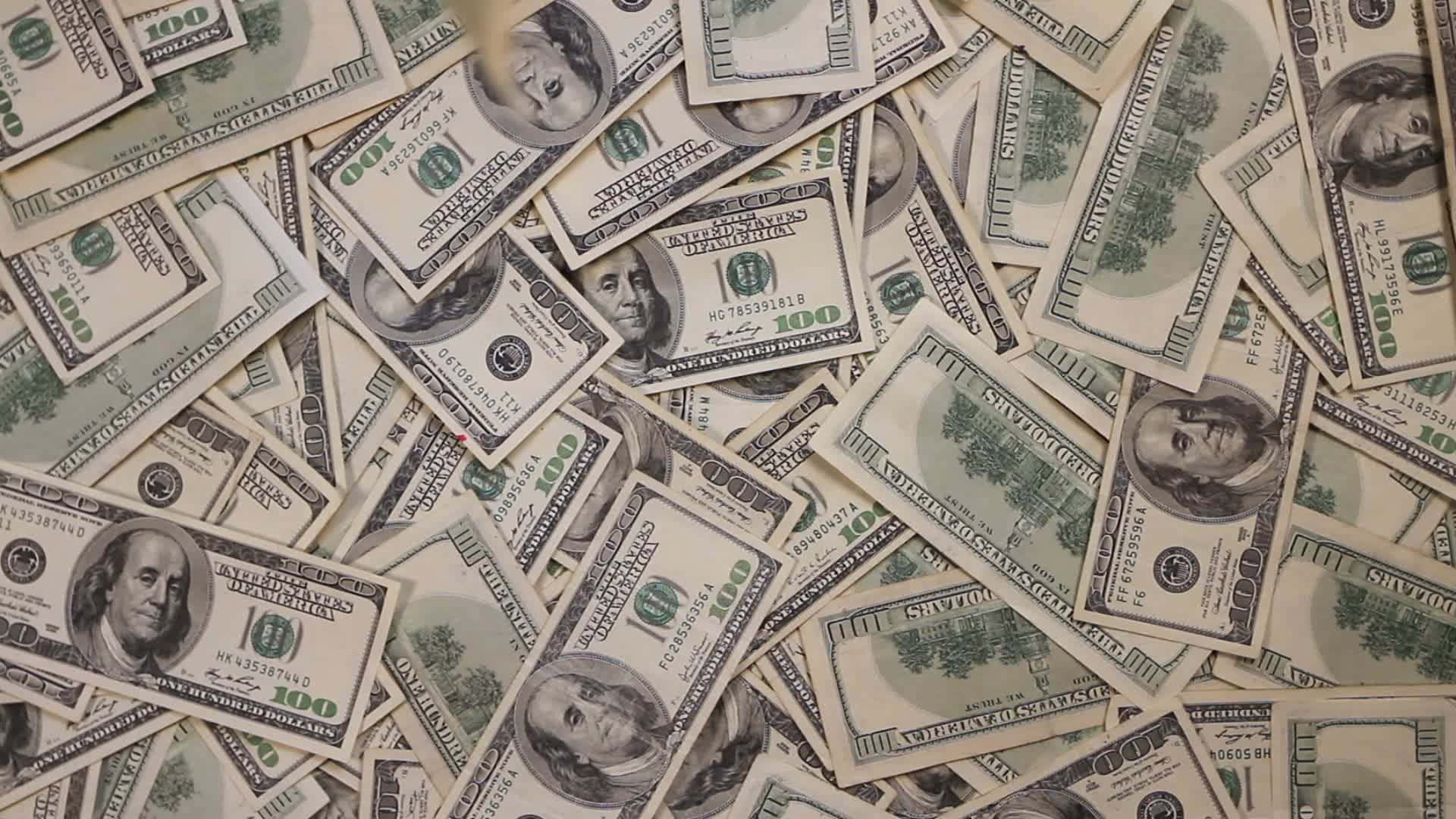 手撿起飄落的鈔票 壁紙 — 一堆散亂的百元美鈔以密集重疊的圖案覆蓋整個畫面。