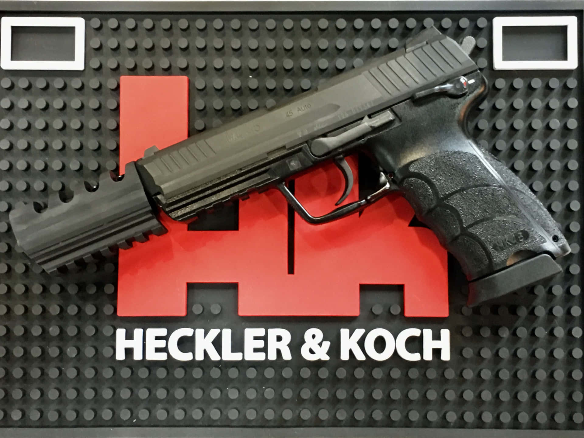 黑色Heckler & Koch手槍放在帶有紅色標誌的品牌展示墊上。