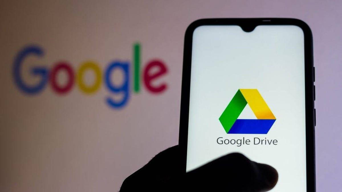 手拿著手機顯示Google Drive應用程式，背景有模糊的Google標誌。