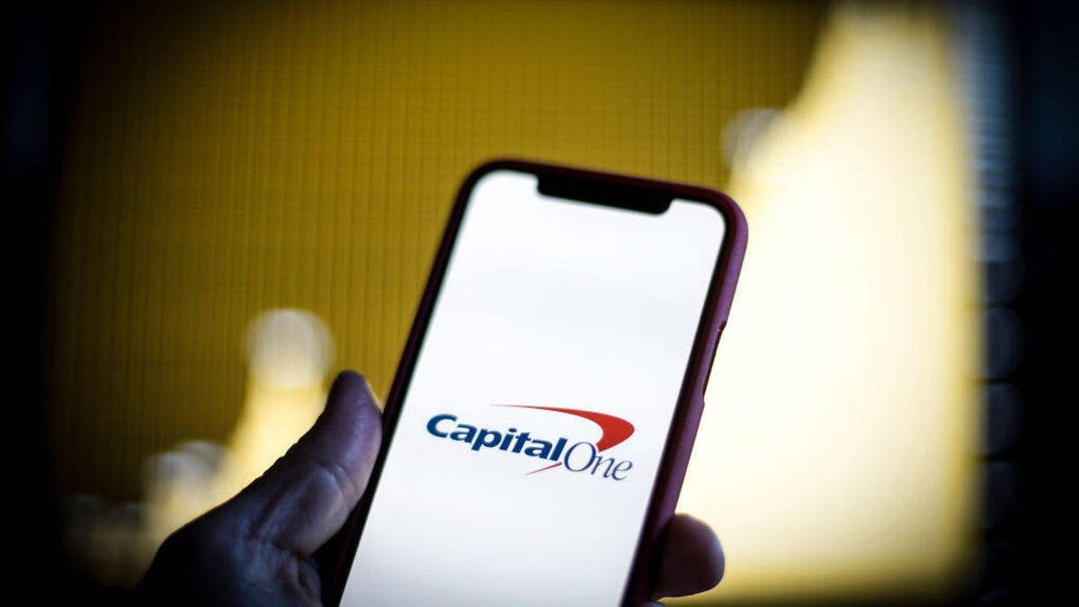 手拿著顯示Capital One標誌的手機，背景溫暖模糊。