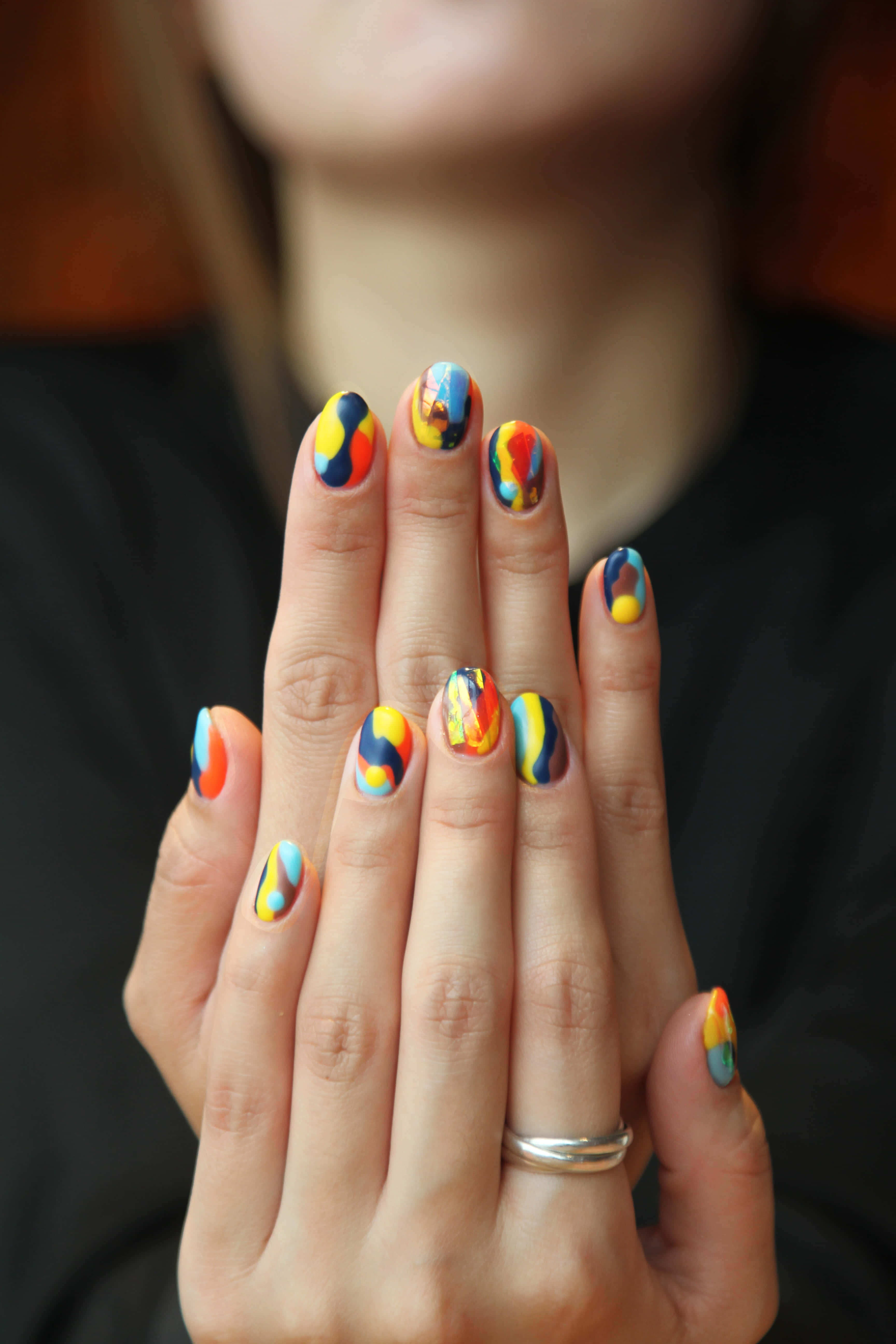 Cute Nails 桌布 壁紙 — 手部特寫，帶有充滿活力的抽象指甲藝術， featuring 大膽的黃、藍、橙和黑色漩渦。