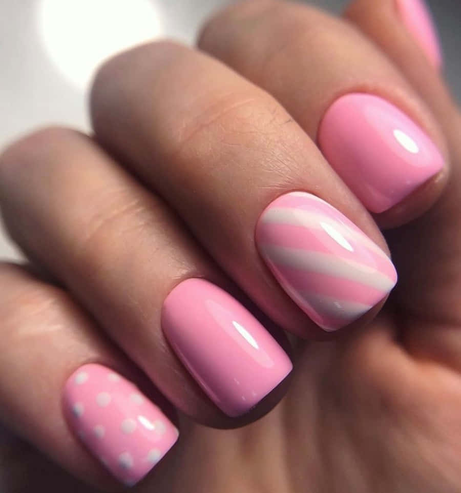 Pink Nail Art 桌布 壁紙 — 手部特寫，帶有光澤粉紅色指甲，飾有白色斜紋和白色圓點，背景柔和模糊。