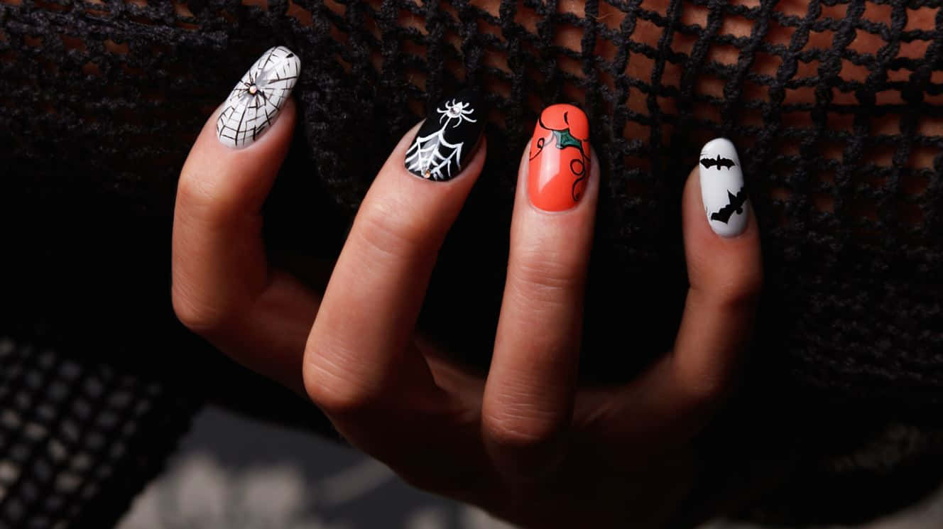 Halloween Nail Art 桌布 壁紙 — 手部特寫，帶有萬聖節主題指甲，飾有蜘蛛、蝙蝠和南瓜，背景為黑色網格。