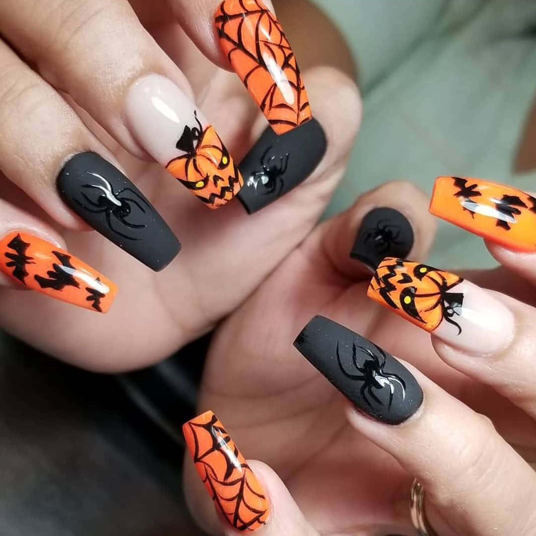 Halloween Nail Art 桌布 壁紙 — 手部特寫，指甲帶有萬聖節主題，在黑色和白色背景上呈現橙色南瓜、蜘蛛和蝙蝠。
