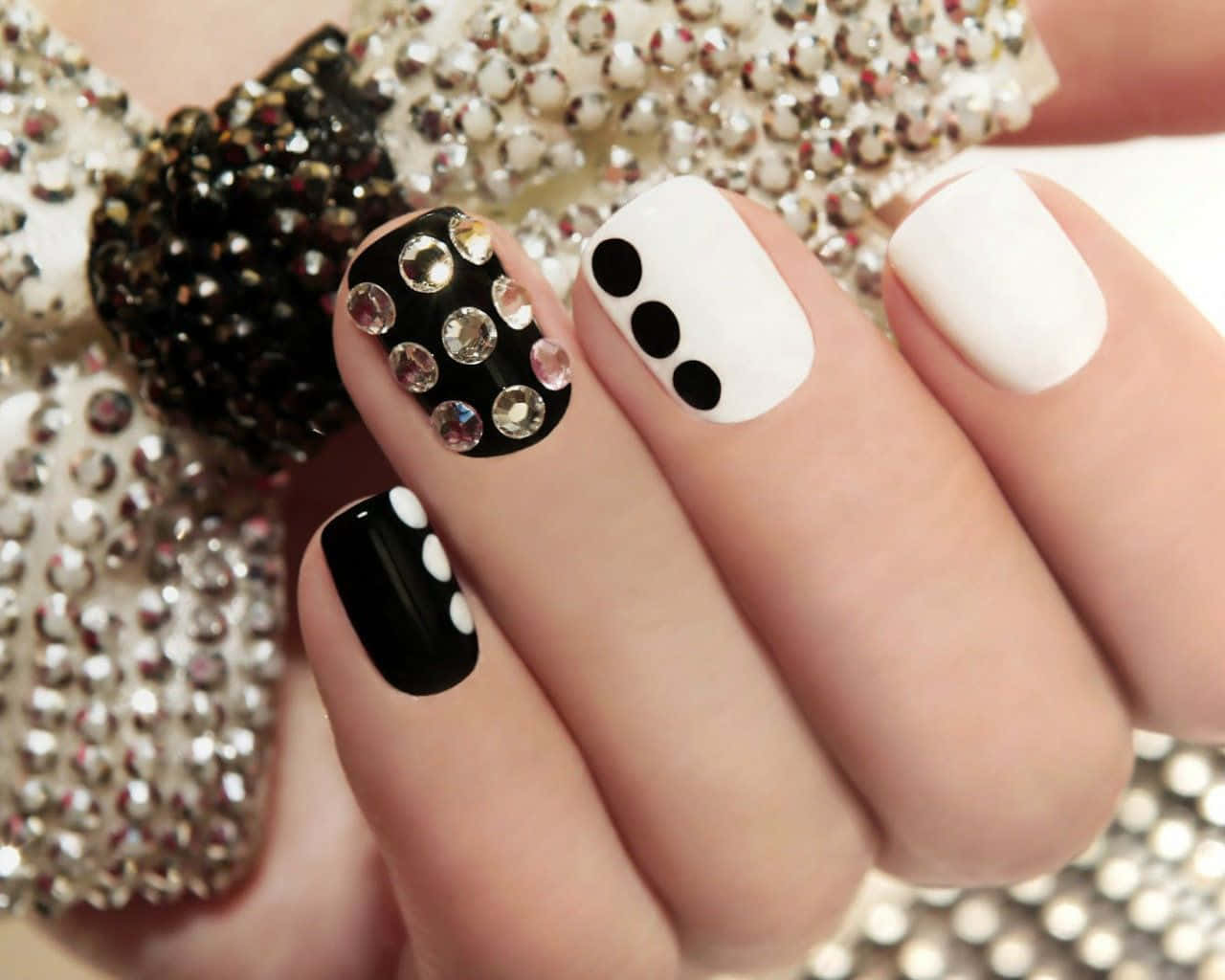 Cute Nails 桌布 壁紙 — 手部特寫，時尚黑白指甲飾有水鑽和圓點，背景是閃亮的水鑽蝴蝶結。