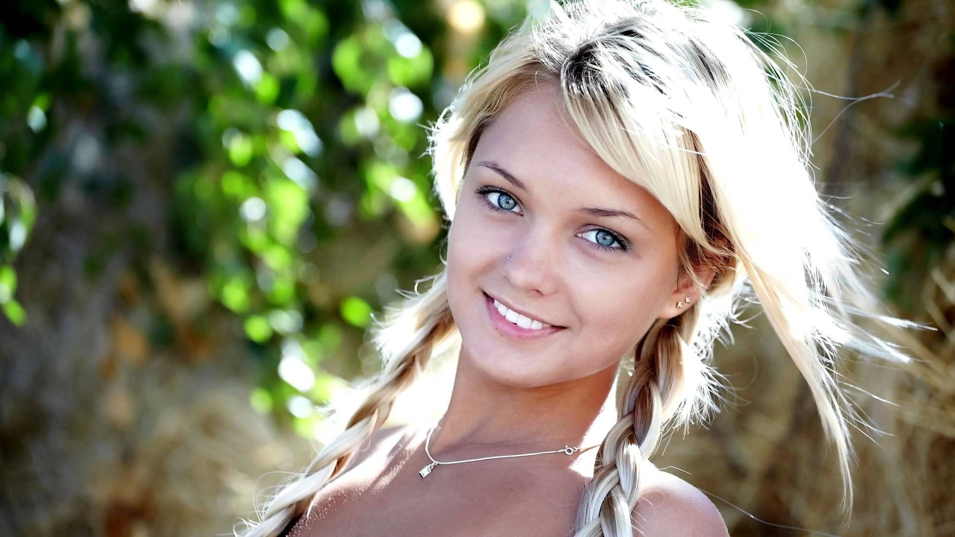 一位微笑的金髮女子，辮子頭髮，在戶外陽光下。