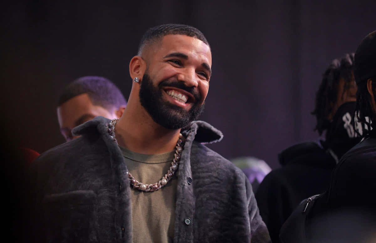 Drake 在昏暗的室內環境中開懷大笑，笑容燦爛。