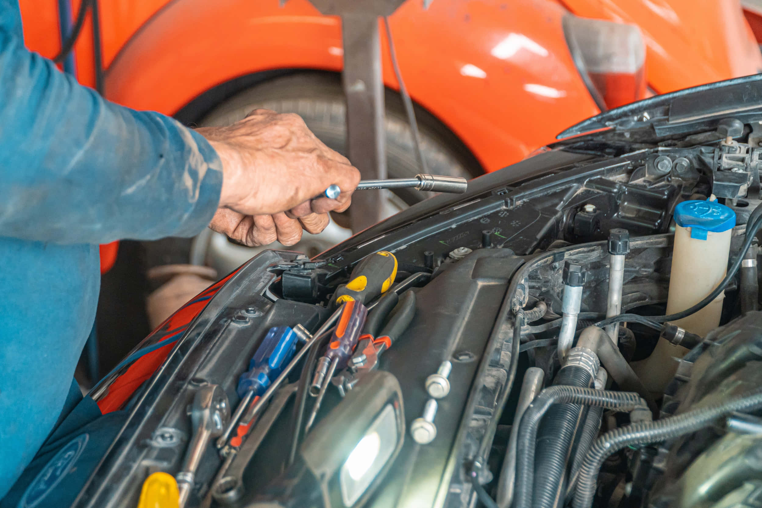 Car Repair 桌布 壁紙 — 技師嘅手喺橙色車嘅引擎艙入面用套筒扳手，引擎艙充滿工具。