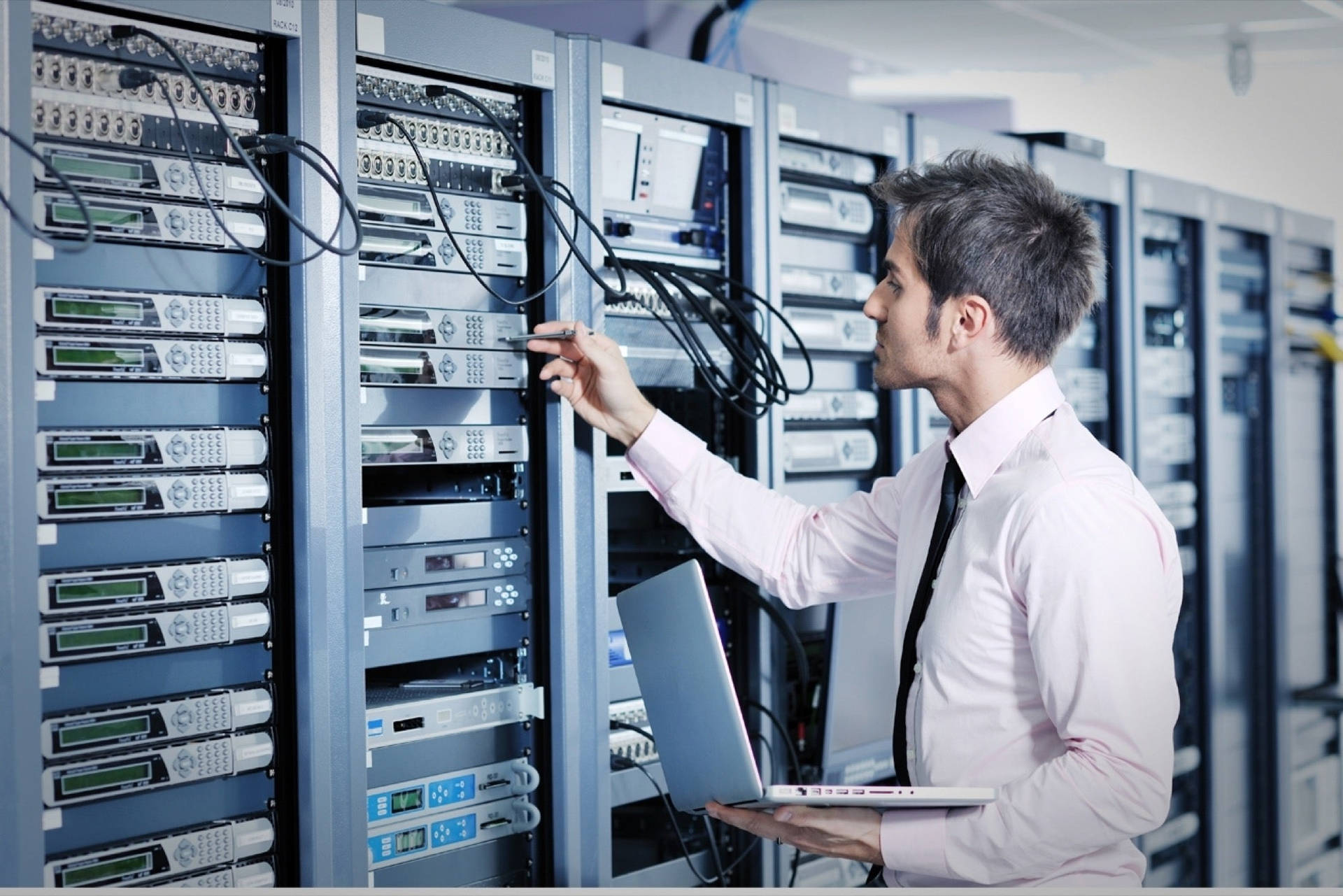 身穿粉紅色襯衫和領帶的男子在手提電腦上操作伺服器機架。