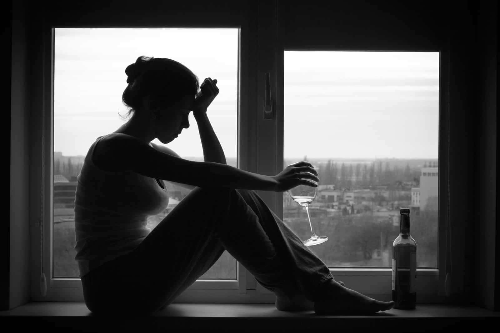 女士坐在窗邊，手持酒杯，旁邊有酒瓶，城市景觀。