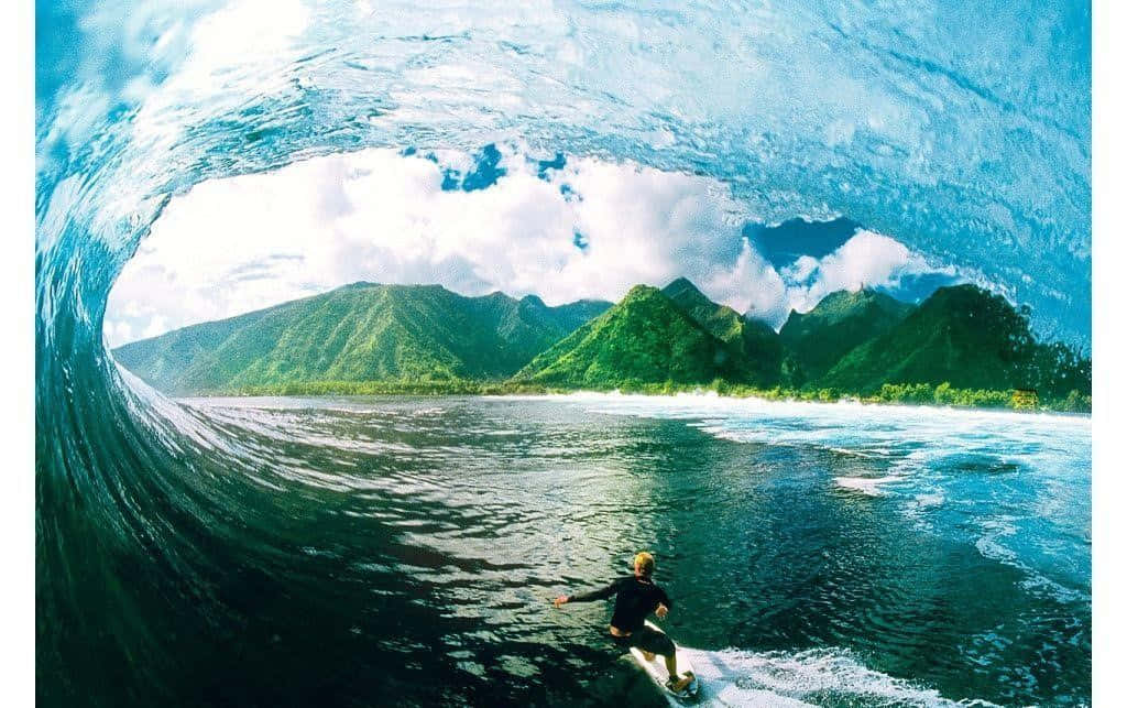 抓住自由的浪花 壁紙 — 一名衝浪者在巨大的藍綠色海浪隧道內乘風破浪，透過彎曲處可見鬱鬱蔥蔥的綠色山脈和多雲的天空。