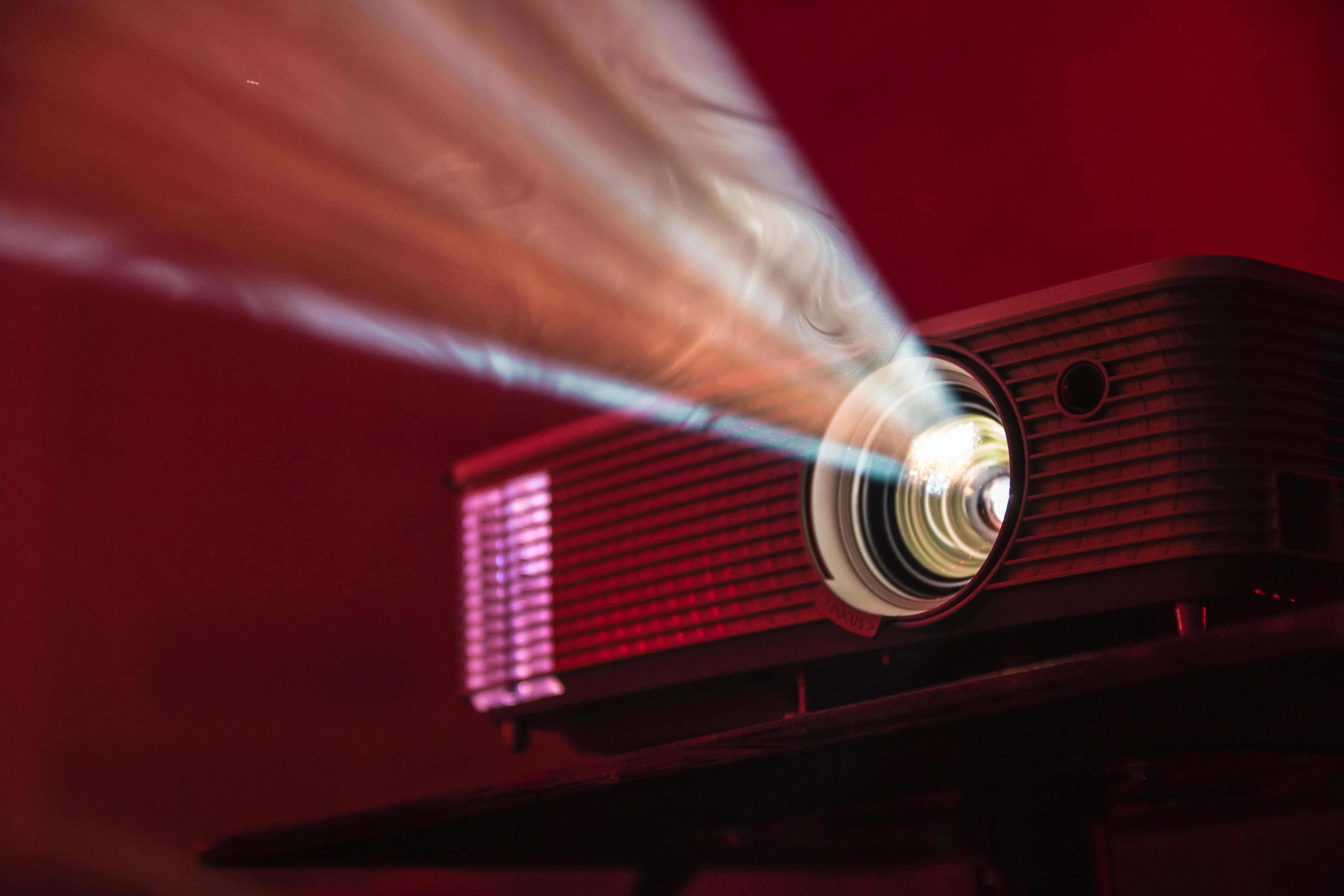 4K Projector 桌布 壁紙 — 投影機的特寫鏡頭，將明亮的光束投射到帶有動態模糊效果的深紅色牆壁上。