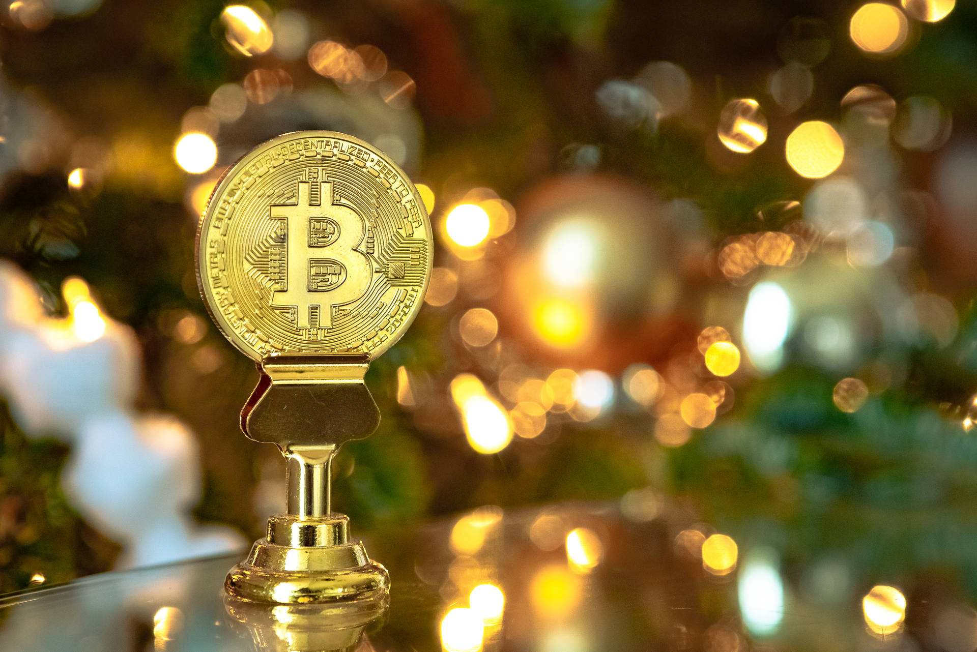 金色比特幣獎盃在反光表面上，背景是模糊的聖誕燈飾。