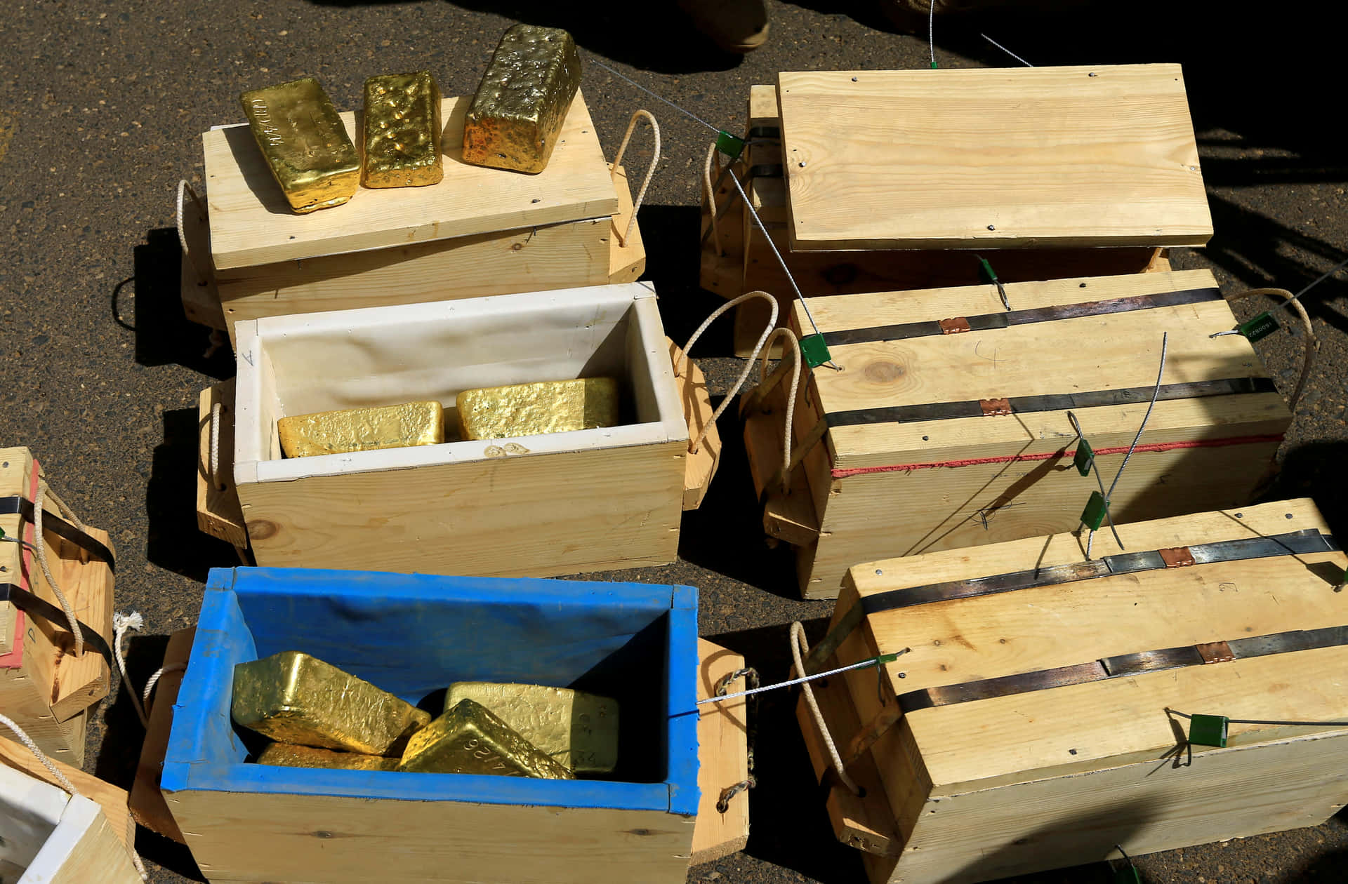 裝滿金條的木箱和藍色容器在瀝青上。