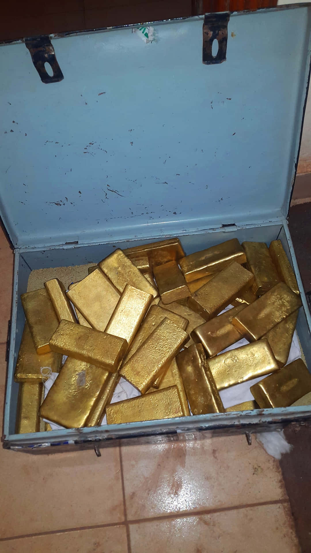 打開的藍色金屬行李箱裝滿金條放在瓷磚地板上。