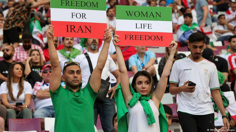 Iran 桌布 壁紙 — 抗議者在體育館內舉著寫有「伊朗自由」和「女性生命自由」的標語，身上披著綠、白、紅三色旗幟。