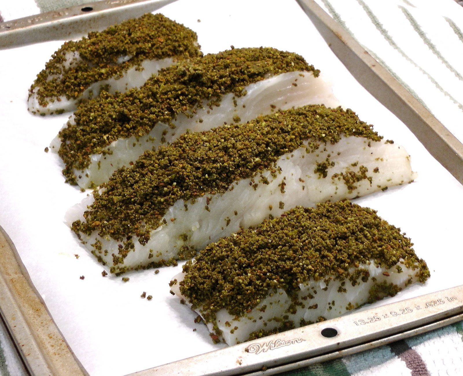 抹茶堅果烤鰈魚 壁紙 — 四塊生魚柳裹上綠色香草外皮，放在金屬烤盤上的烘焙紙上。