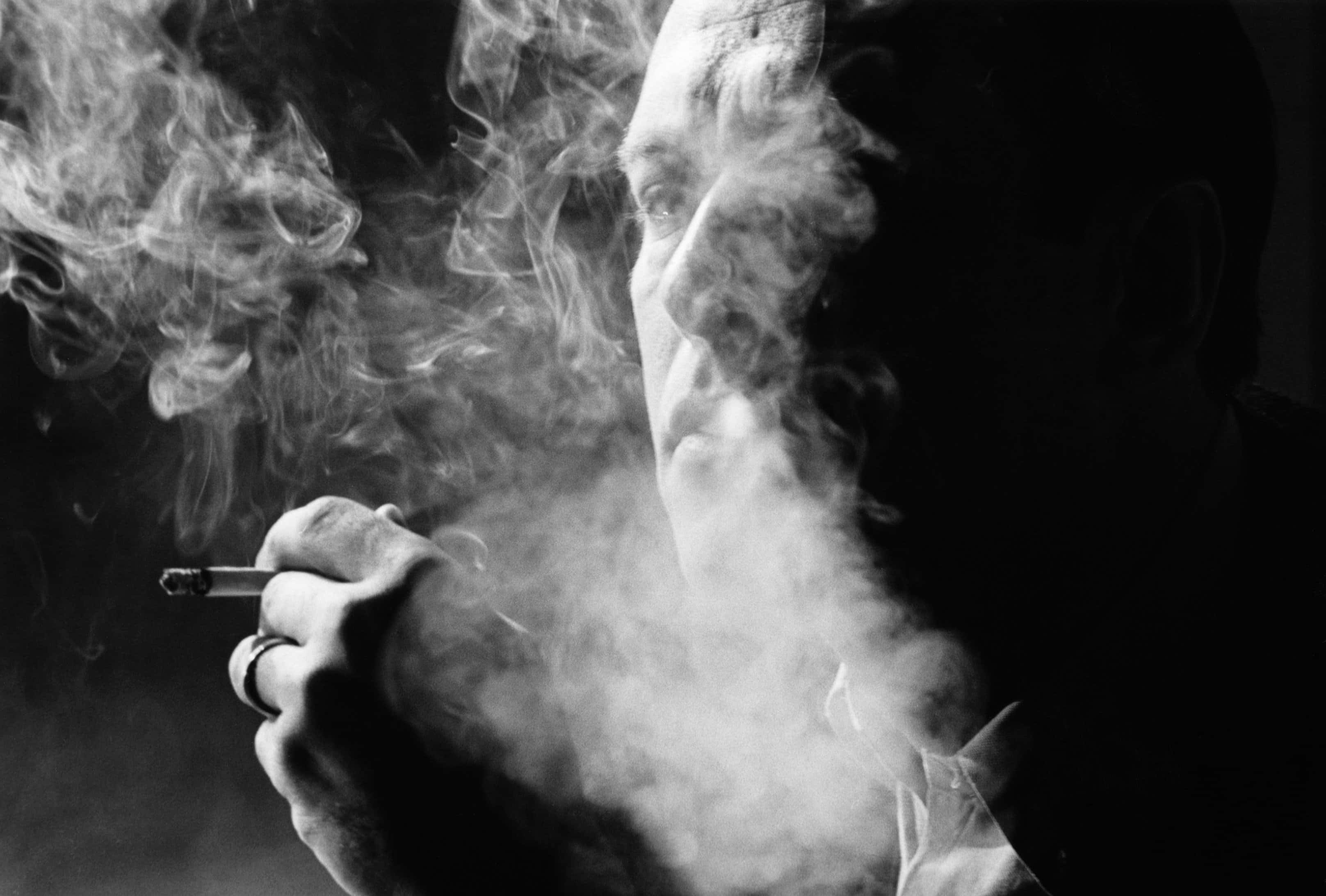 抽根煙，放鬆一下 壁紙 — 陰影中的男人呼出濃煙，手持香煙，呈現清晰的黑白肖像。