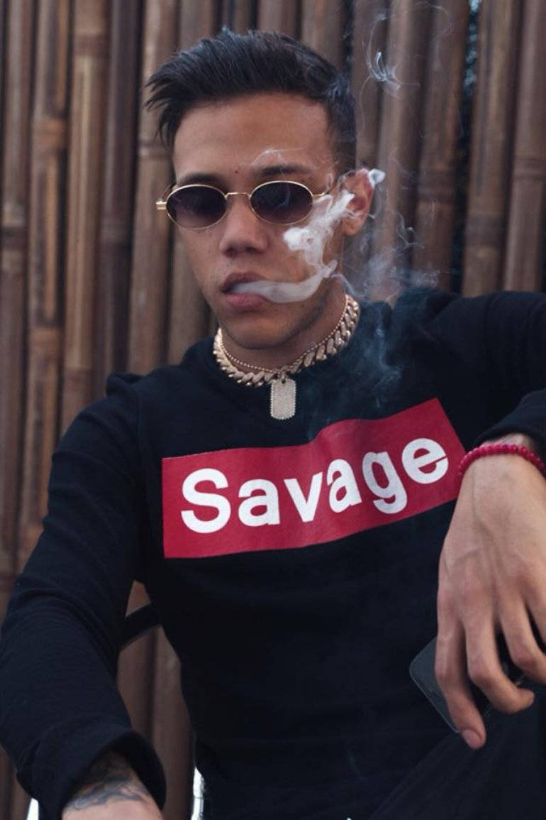 年輕男子戴太陽眼鏡和 'Savage' 連帽衫在竹牆附近吸煙。