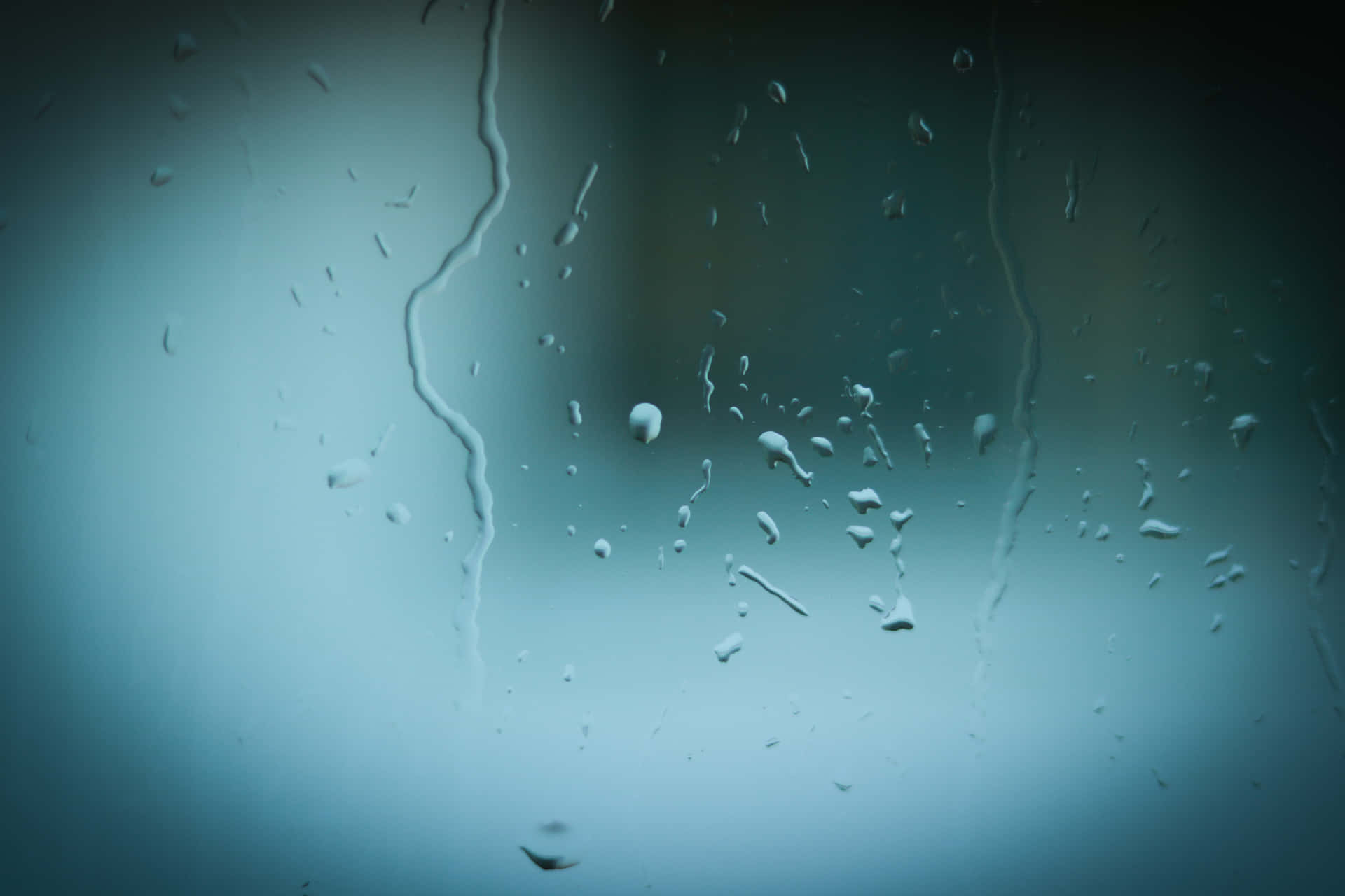 雨滴在玻璃窗上滑落，背景是模糊的藍色。
