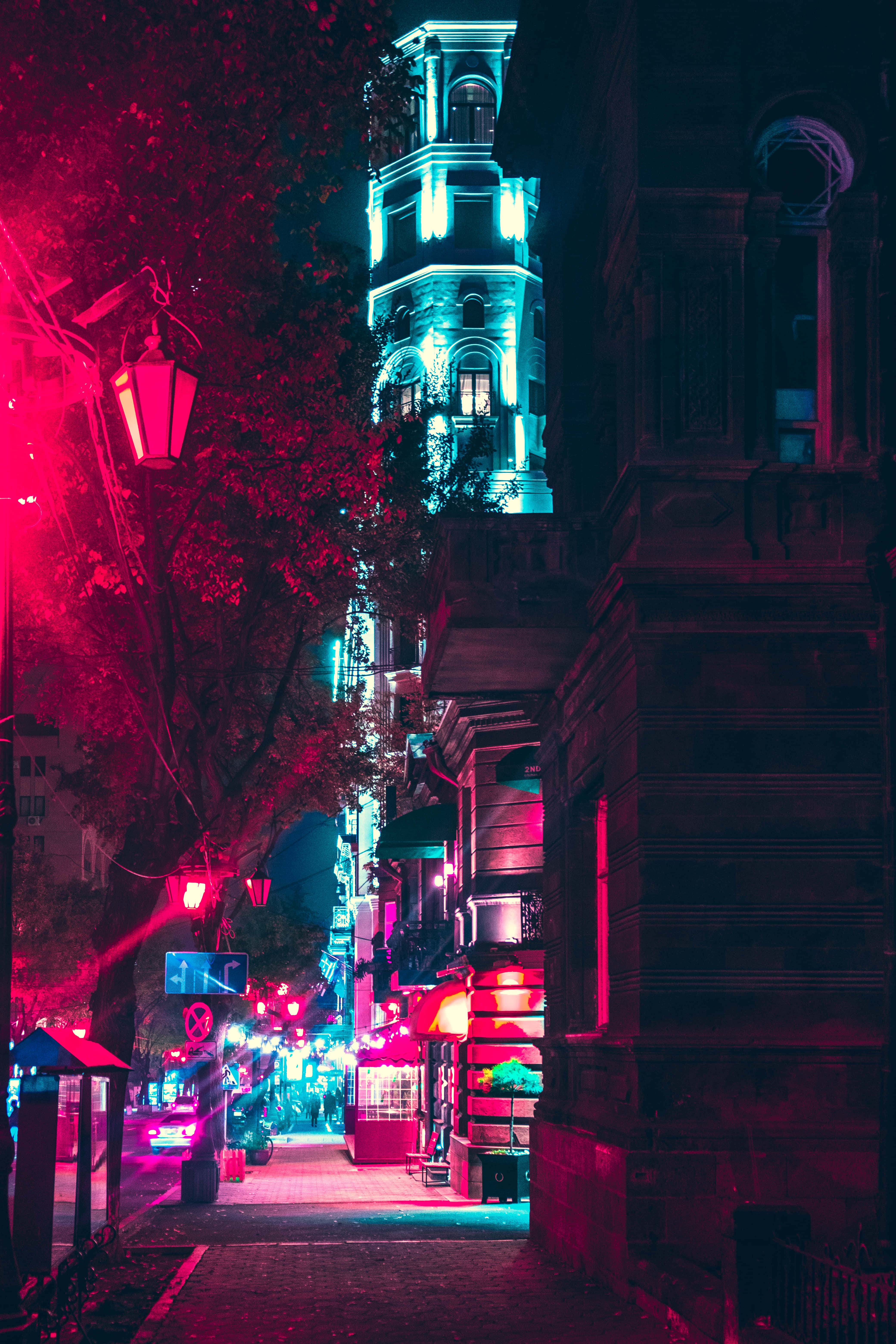 抽象呈現熱鬧的城市夜景 壁紙 — 夜晚狹窄的城市小巷，被街燈和高聳建築物的鮮豔紅色和青色霓虹燈光沐浴。