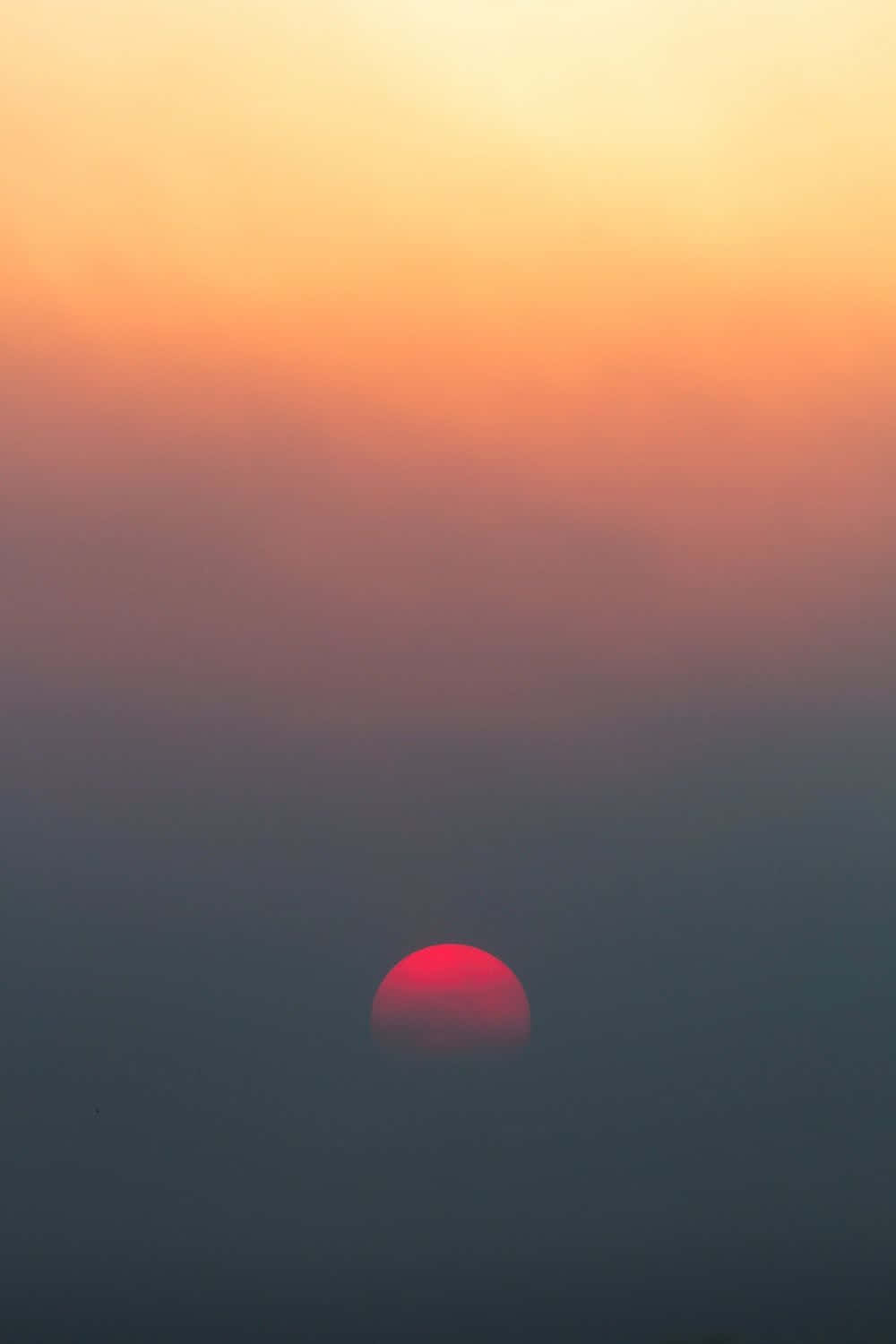 紅色太陽在薄霧後落下，天空呈現橙色和紫色