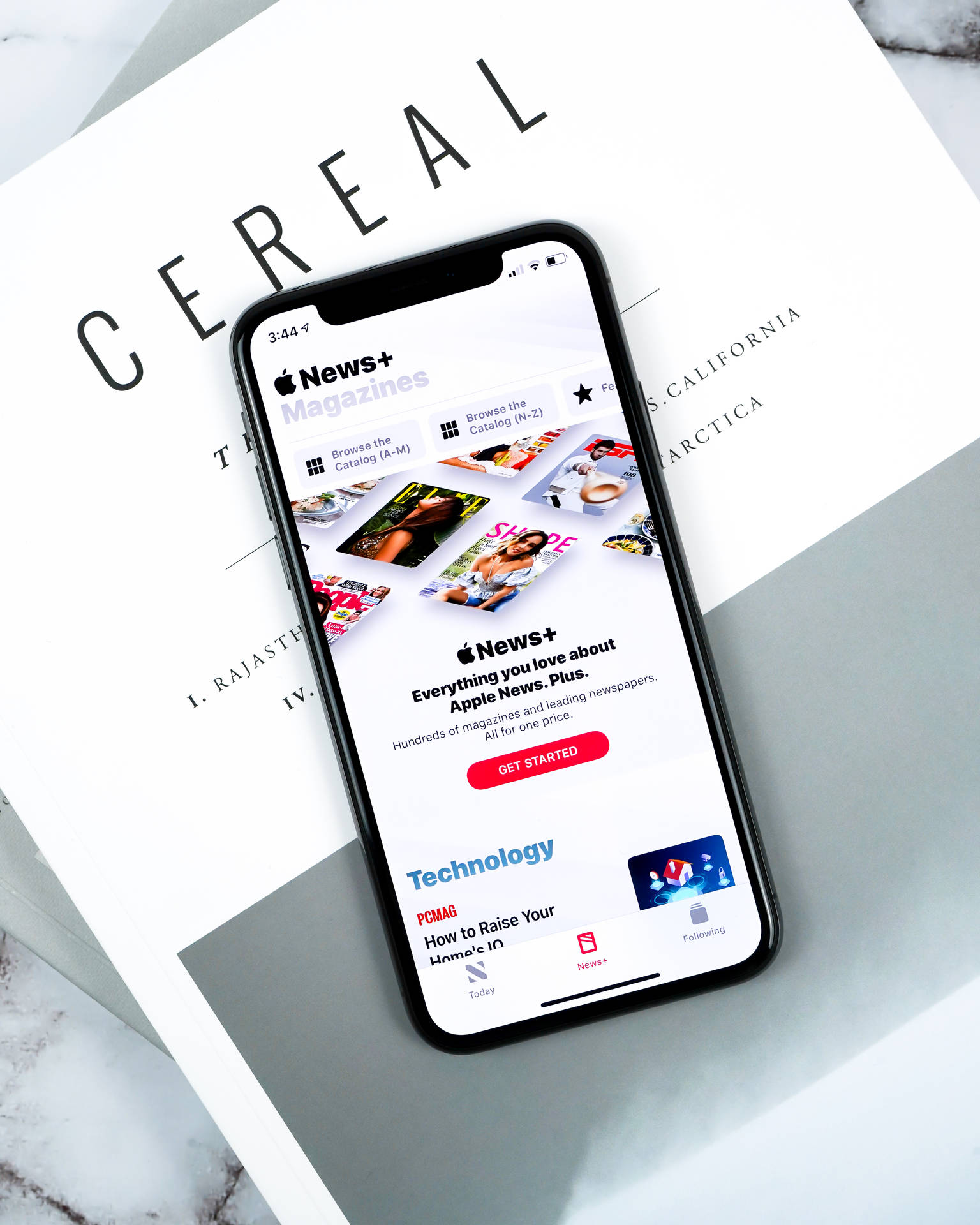 智能手機在大理石表面上顯示 Apple News+ 應用程式，旁邊有一本白色書本名為 CEREAL。