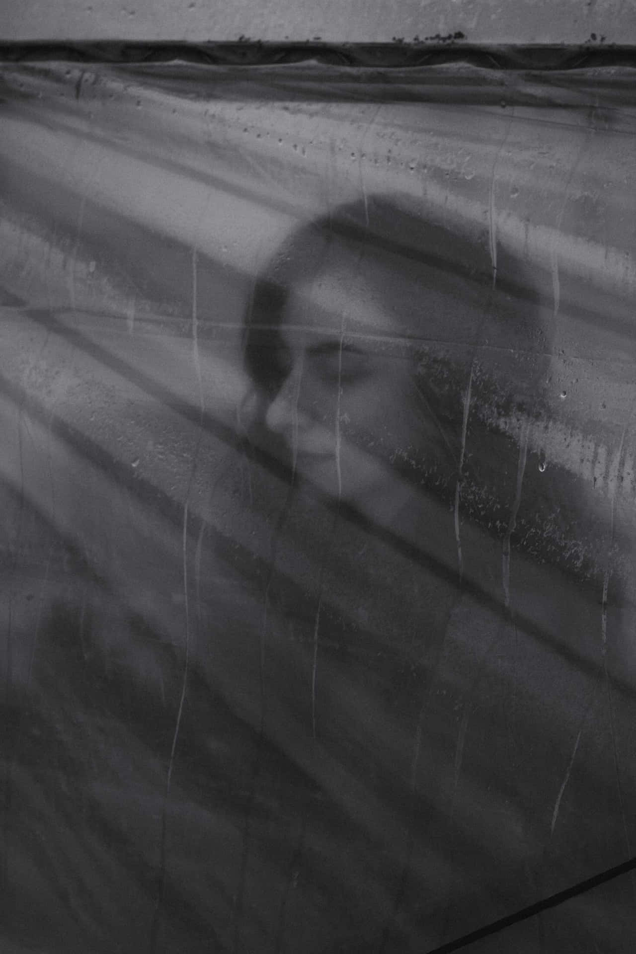 透過雨水濕潤的玻璃看到的女人臉龐，伴隨著柔和的光線。