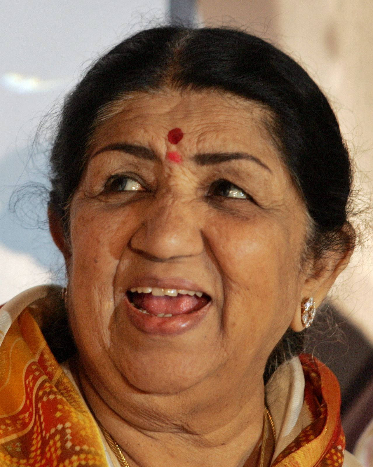 拉塔·曼格什卡 - 真誠微笑 壁紙 — Lata Mangeshkar 的近照，她額頭上有紅色吉祥痣，戴著圖案橙色圍巾，溫暖微笑。