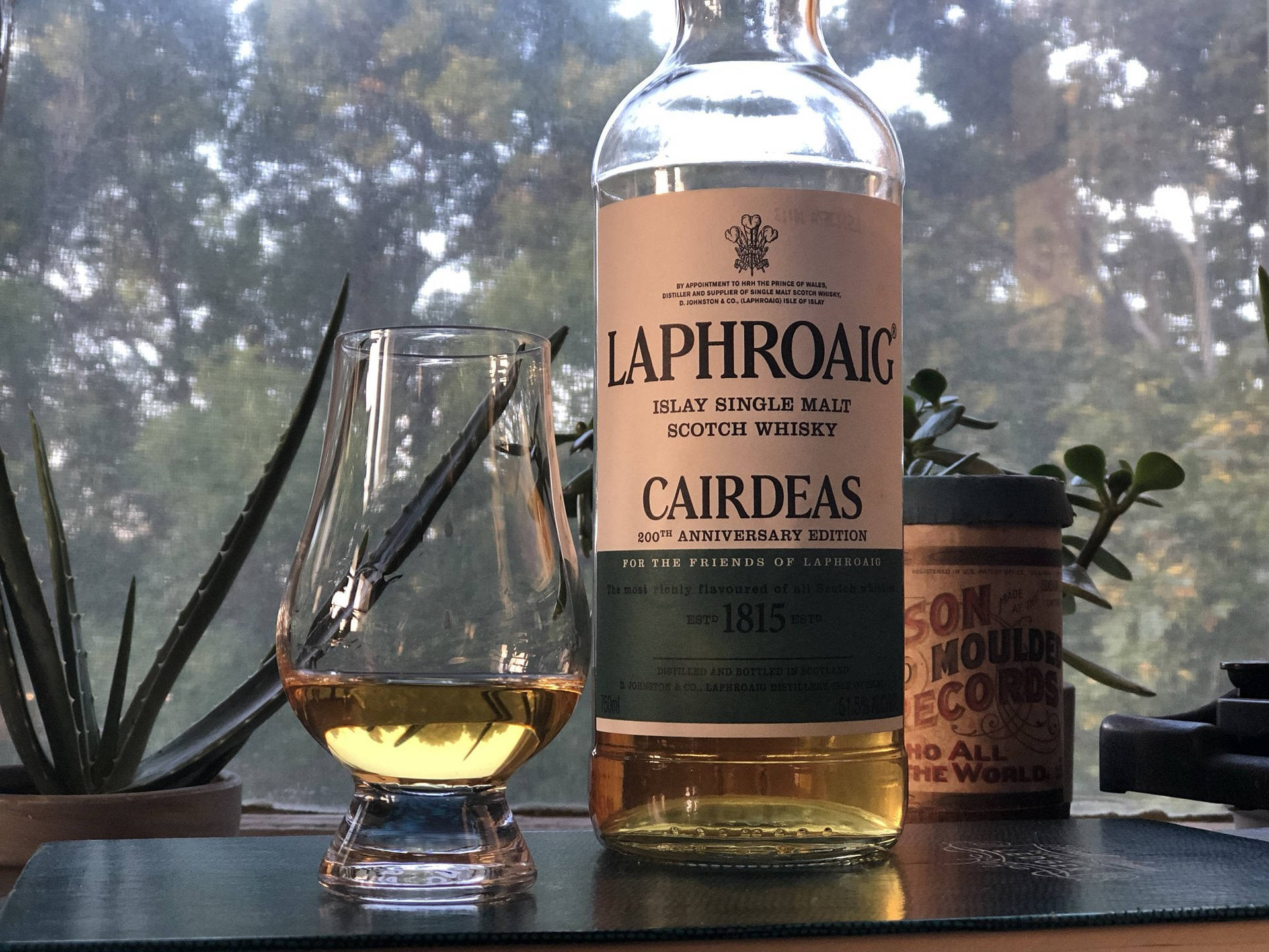 一瓶Laphroaig威士忌和品酒杯放在有植物的窗台上。