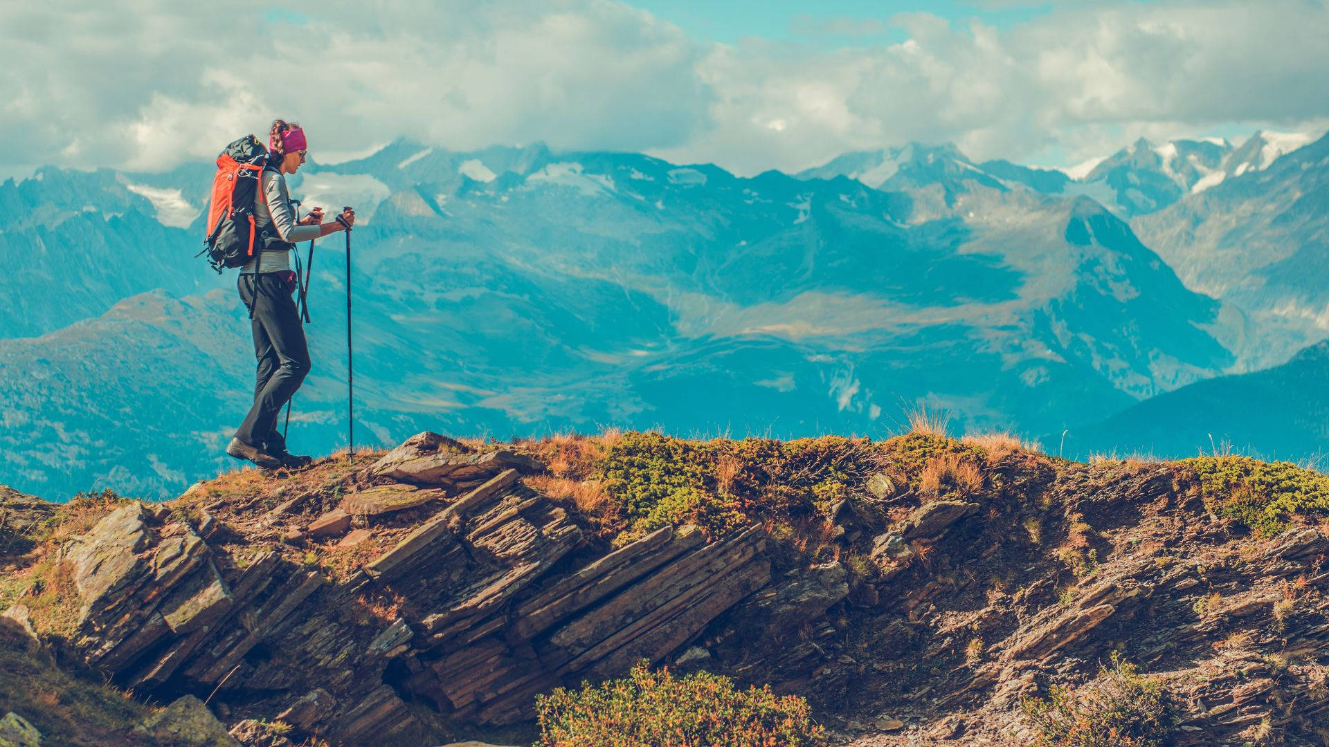 背著紅色背包的遠足者站在山脊上，眺望遠方的山峰。
