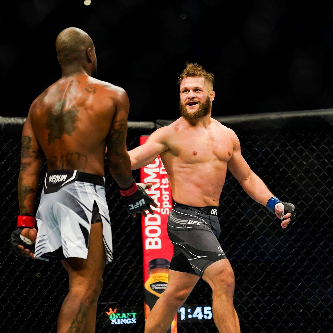 拉斐爾·菲茲耶夫對戰鮑比·格林 壁紙 — 兩名男性MMA拳手在籠中，一人咧嘴大笑，同時向背對鏡頭、露出紋身的另一人伸出手。