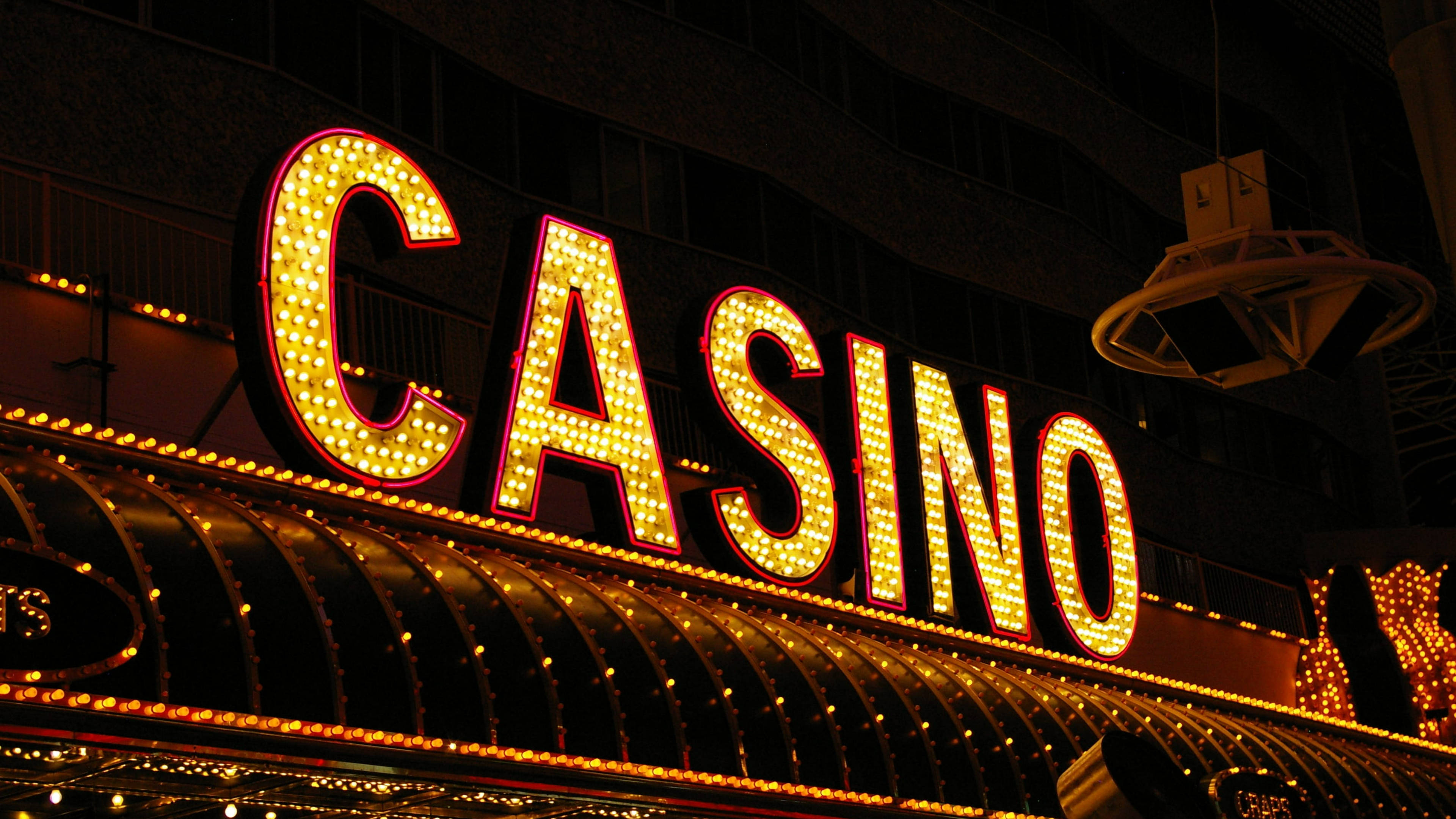 拉斯維加斯夜景全景 壁紙 — 一個耀眼的霓虹燈「CASINO」招牌在漆黑的都市夜空下溫暖地發光，下方有彎曲的遮陽篷。