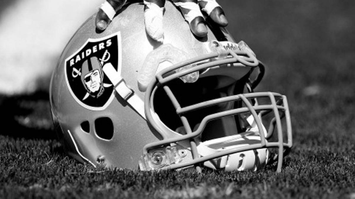 Raiders 美式足球頭盔放在草地上，戴手套的手握住它。