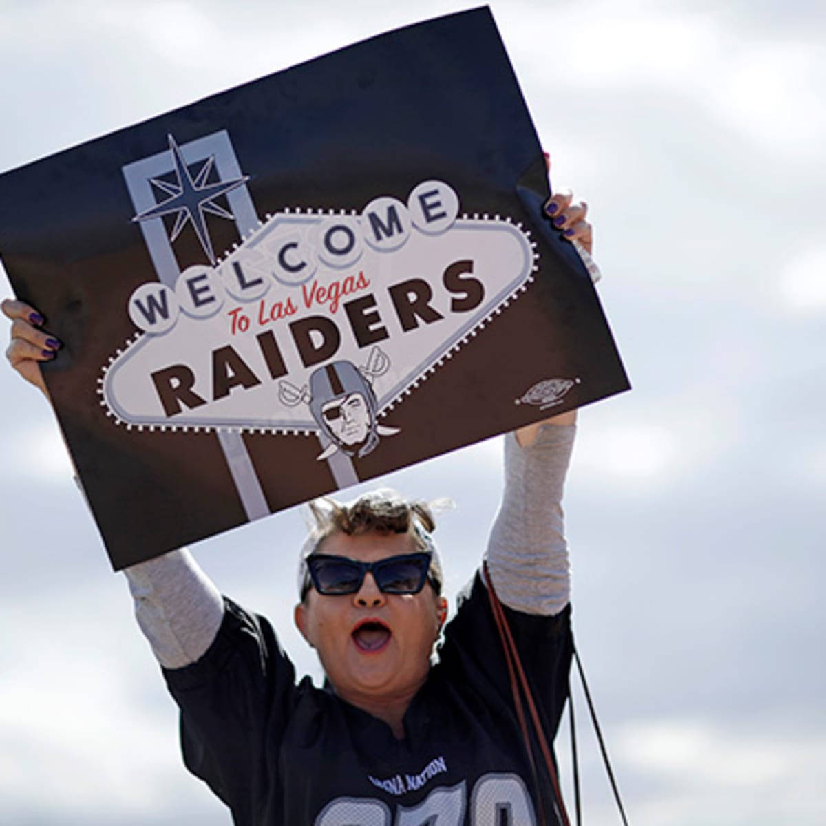 一名戴太陽眼鏡的人士在戶外舉起 Raiders 歡迎標誌。