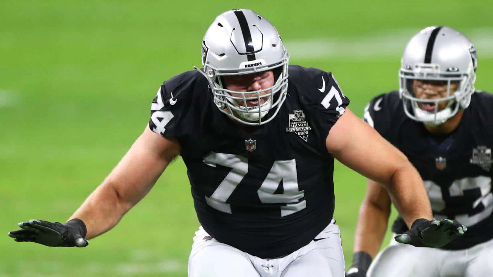 NFL美式足球員穿著黑色和銀色制服在綠色場地上奔跑。