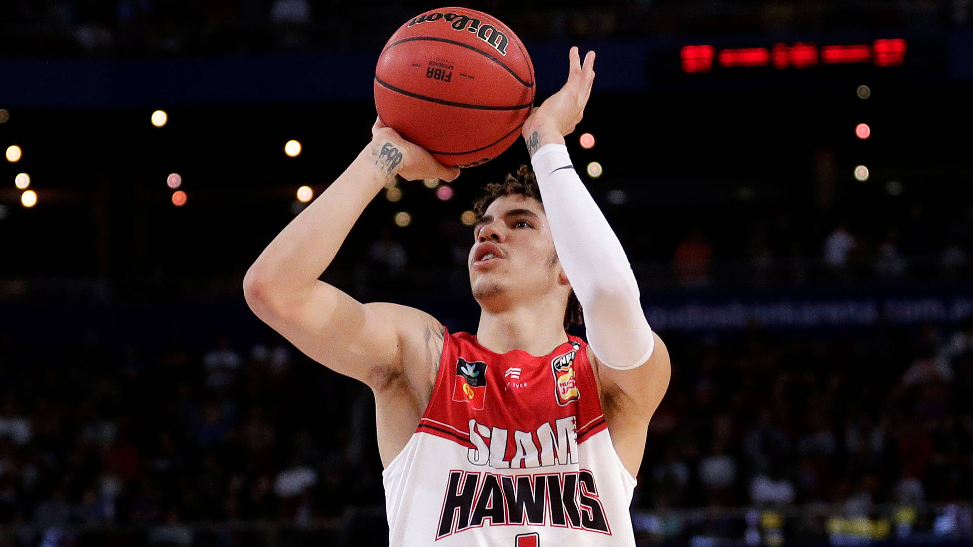 拉梅洛·鮑爾投籃 壁紙 — 一名身穿紅白『SLAM HAWKS』球衣的籃球運動員在場館燈光下投出紅色Wilson球，背景有模糊的觀眾。