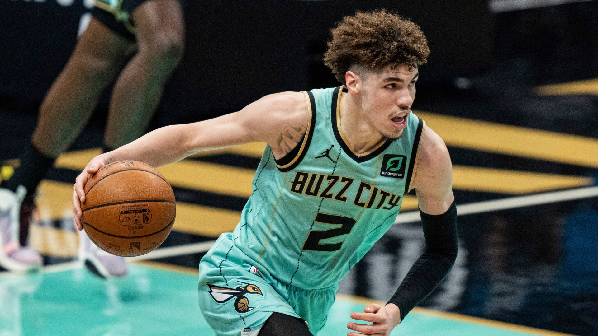 拉梅洛·鲍尔持球奔跑 壁紙 — 一名身穿青綠色「Buzz City」球衣的籃球運動員在明亮的場館燈光下於比賽中激烈運球。