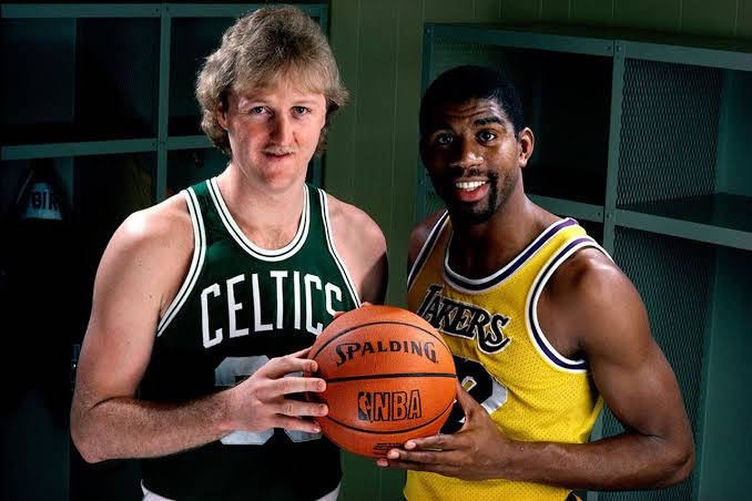 兩位身穿復古球衣的NBA籃球運動員在更衣室裡拿著一個籃球。