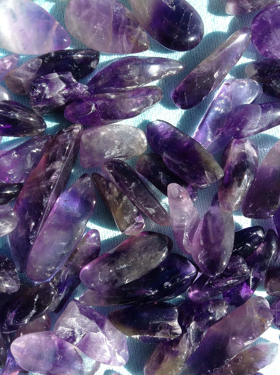 Amethyst 桌布 壁紙 — 拋光紫水晶晶體的近距離特寫，呈現不同深淺的紫色，放置在淺藍色紋理表面上。