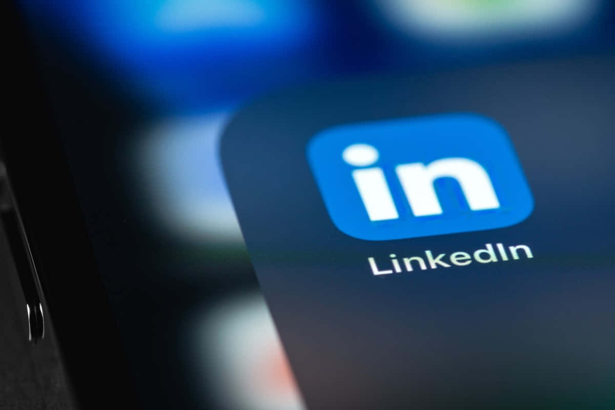 拓展你的網絡 壁紙 — LinkedIn 應用程式圖標在智能手機屏幕上發光的特寫，背景應用程式模糊。