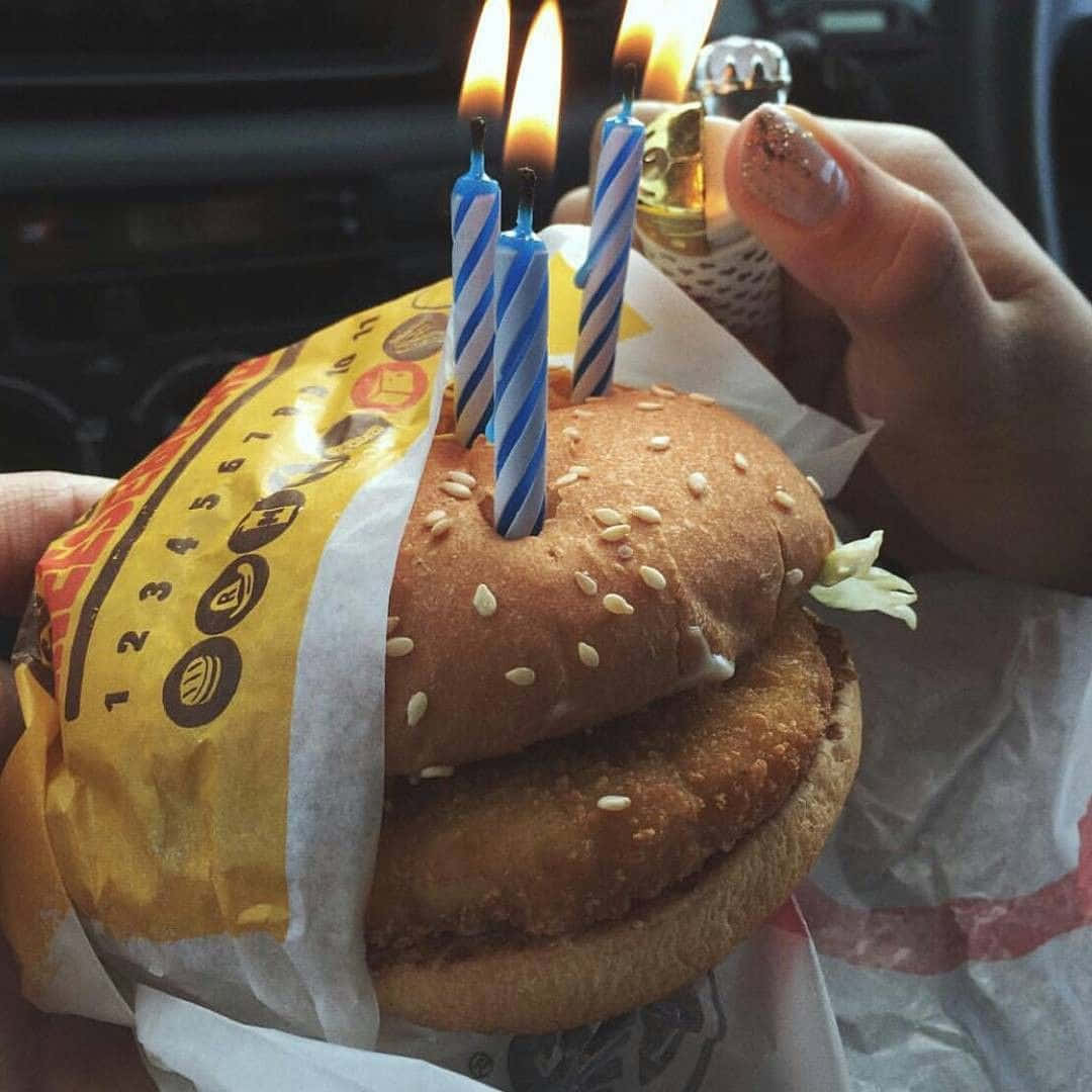 手在黃色紙包裹的漢堡上點燃生日蠟燭。