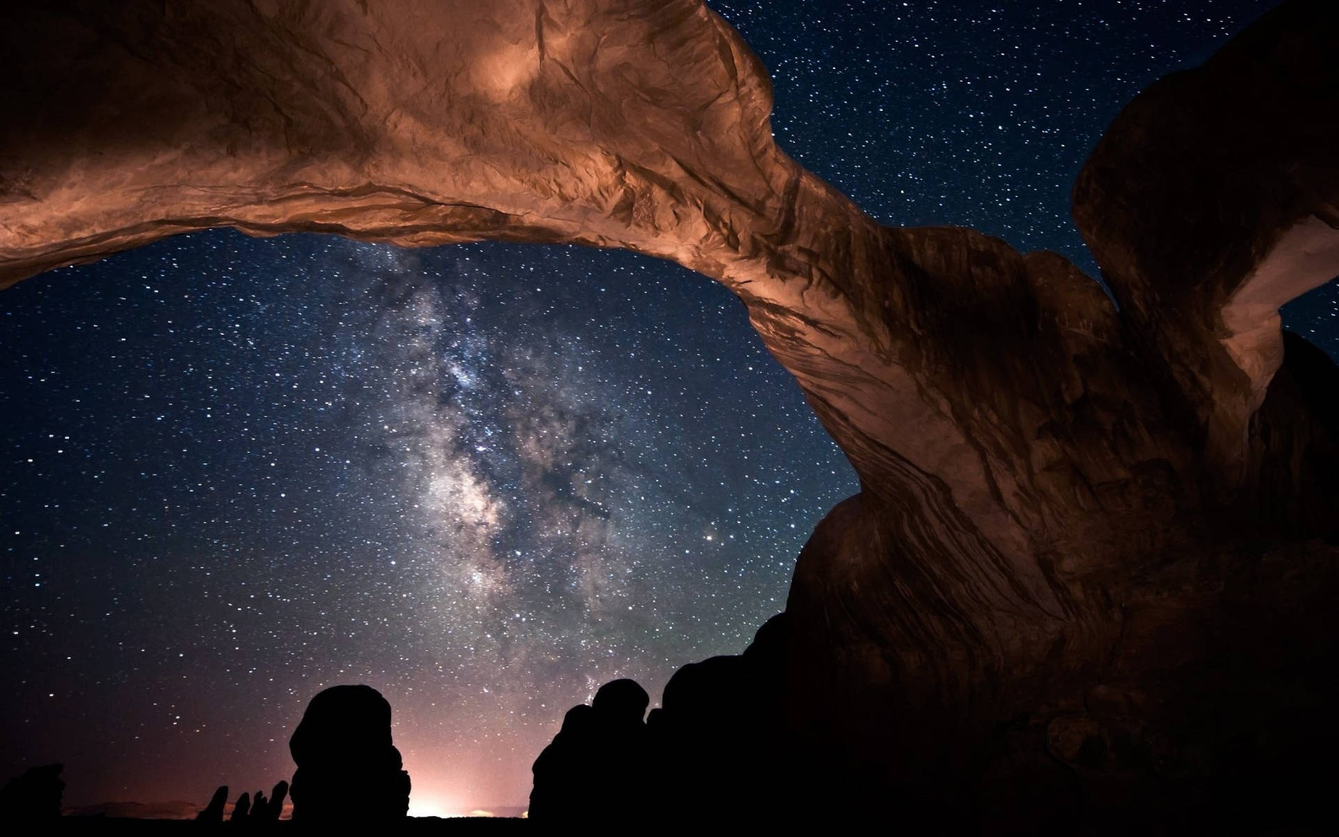剪影人物在夜間透過天然石拱觀賞銀河。