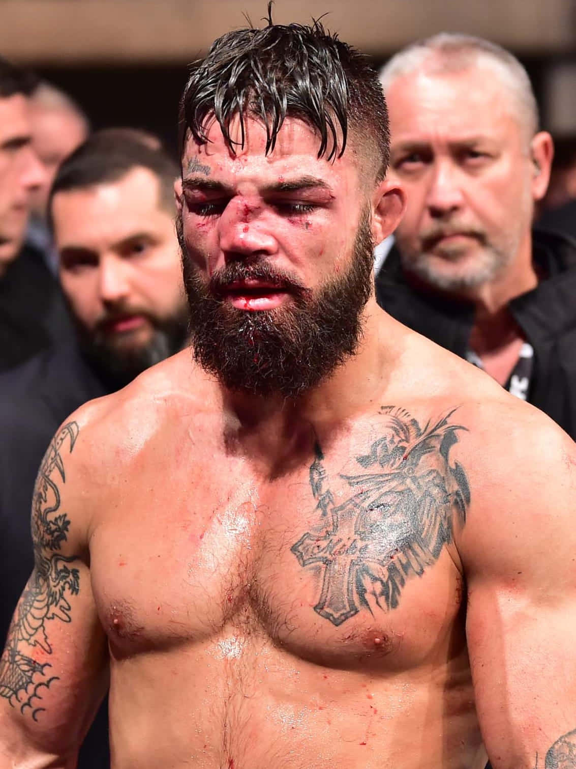 拳擊賽後受傷的MMA選手 壁紙 — 一名滿身鮮血、留鬍子、有紋身的戰士在官員包圍下，於一場殘酷比賽後凝視著。