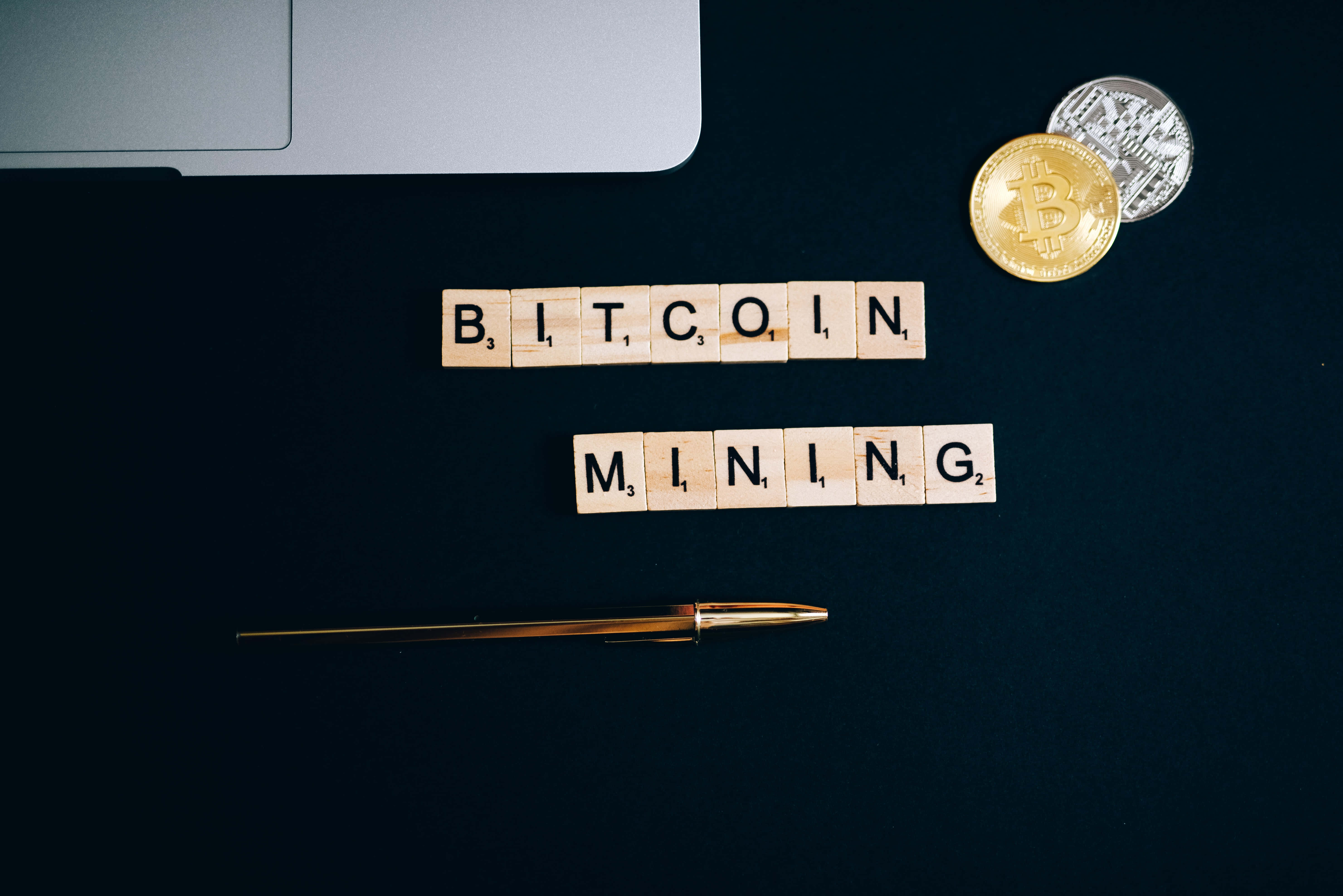 Mining 桌布 壁紙 — 拼出 bitcoin mining 的木製字母塊放在硬幣和手提電腦旁邊的深色表面上。