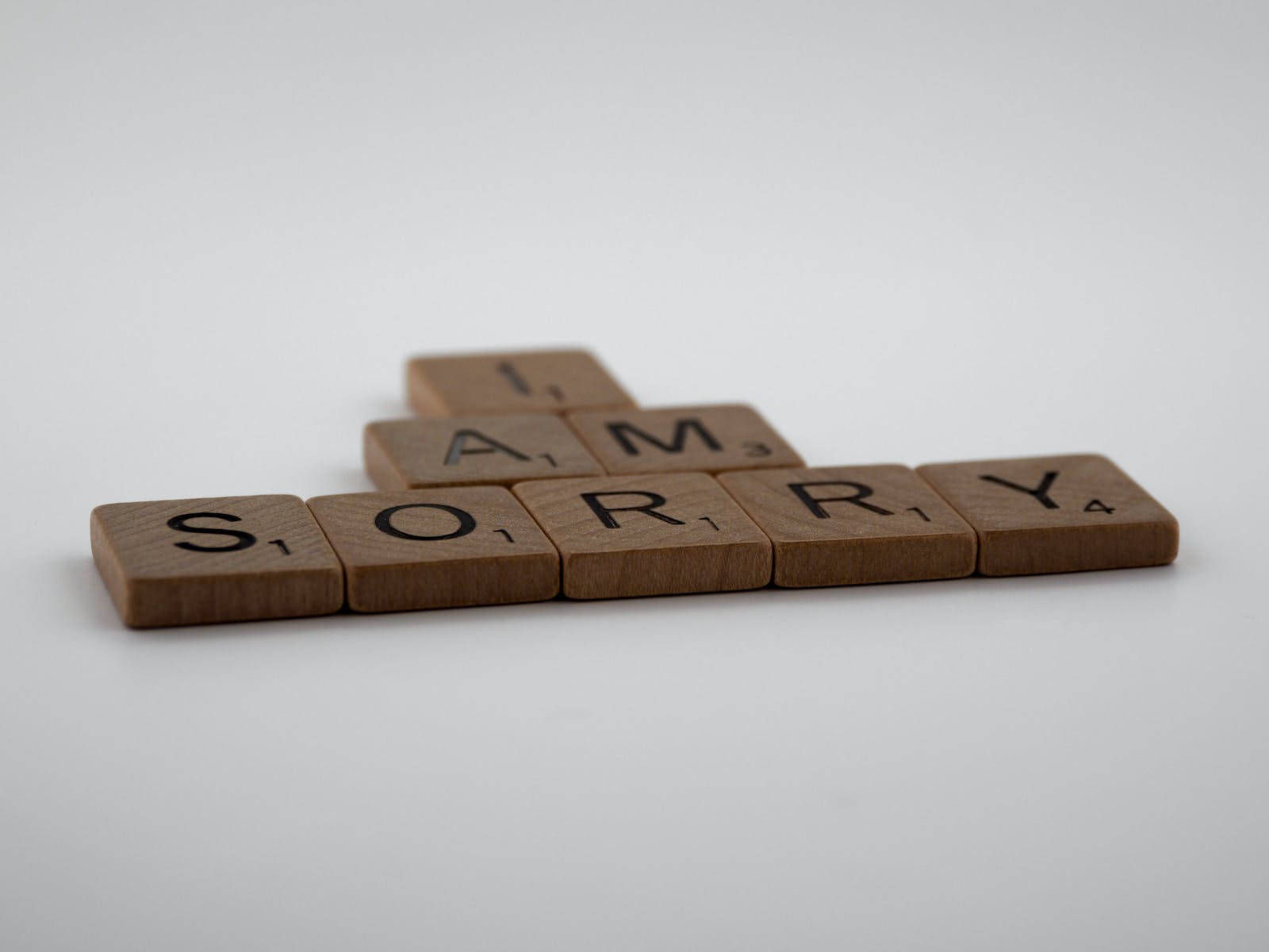 拼字遊戲拼出「我道歉」 壁紙 — 木製Scrabble字母牌拼出「I AM SORRY」，以金字塔形排列在純白表面上。