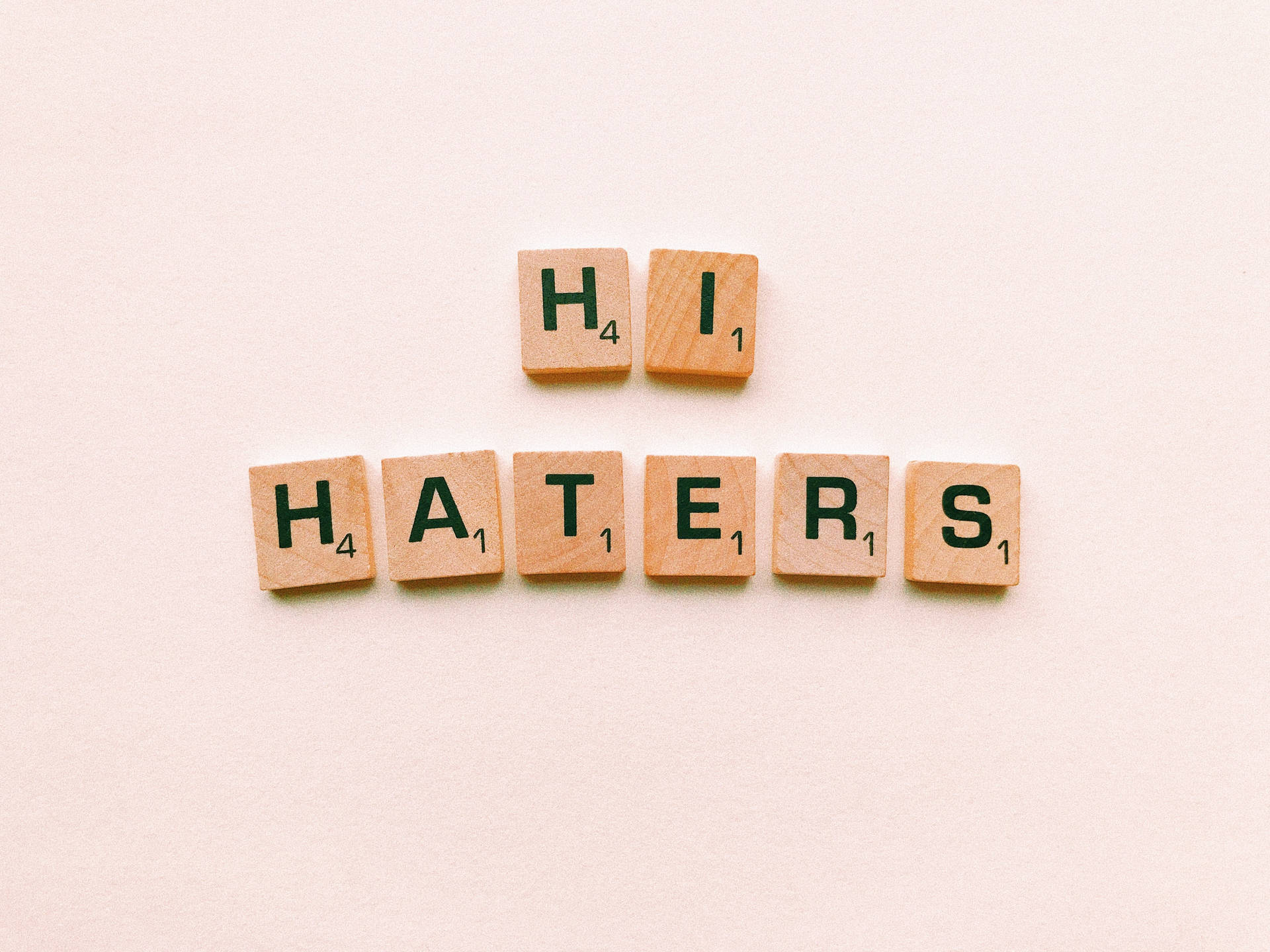 木製 Scrabble 字母牌在米色背景上拼出「Hi Haters」。